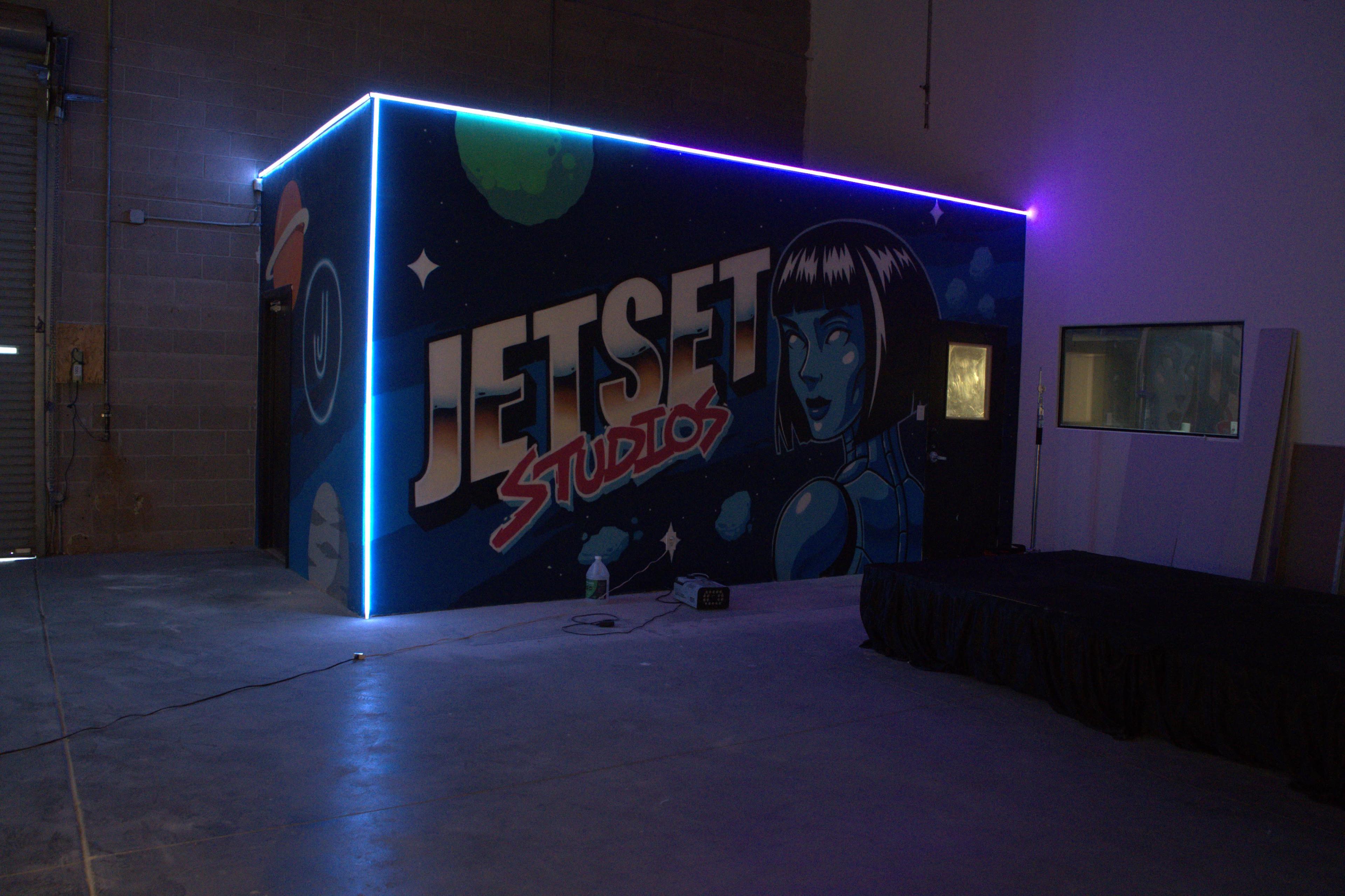 The image shows a brightly colored mural on a studio wall featuring the text "JETSET STUDIOS" alongside a futuristic female character, illuminated by neon lights.