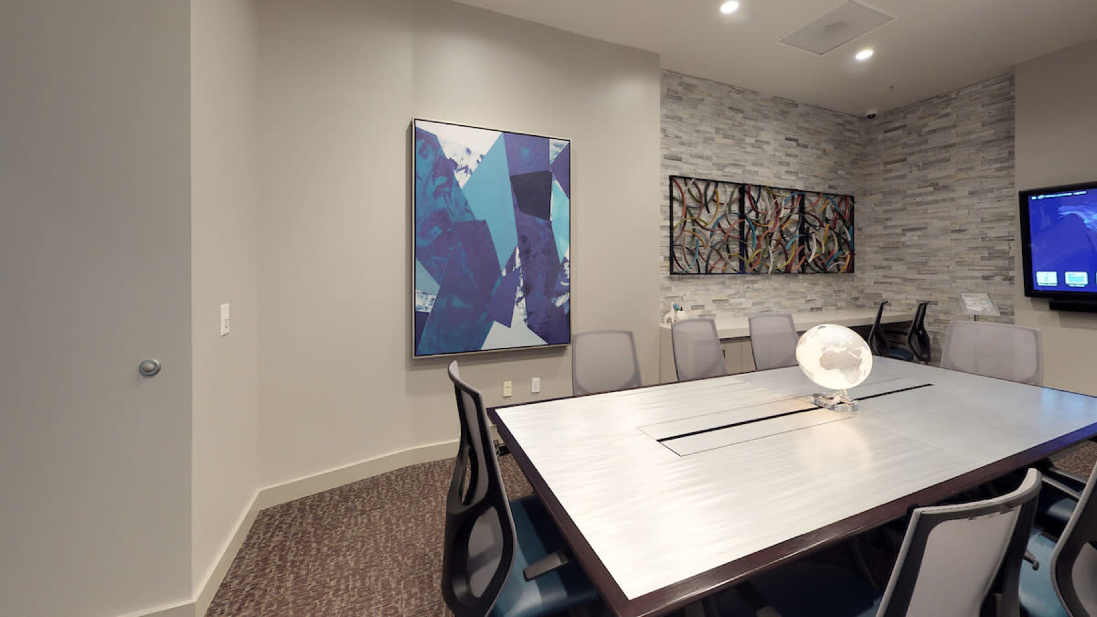 A modern conference room featuring a large table, abstract artwork on the walls, and a television screen.