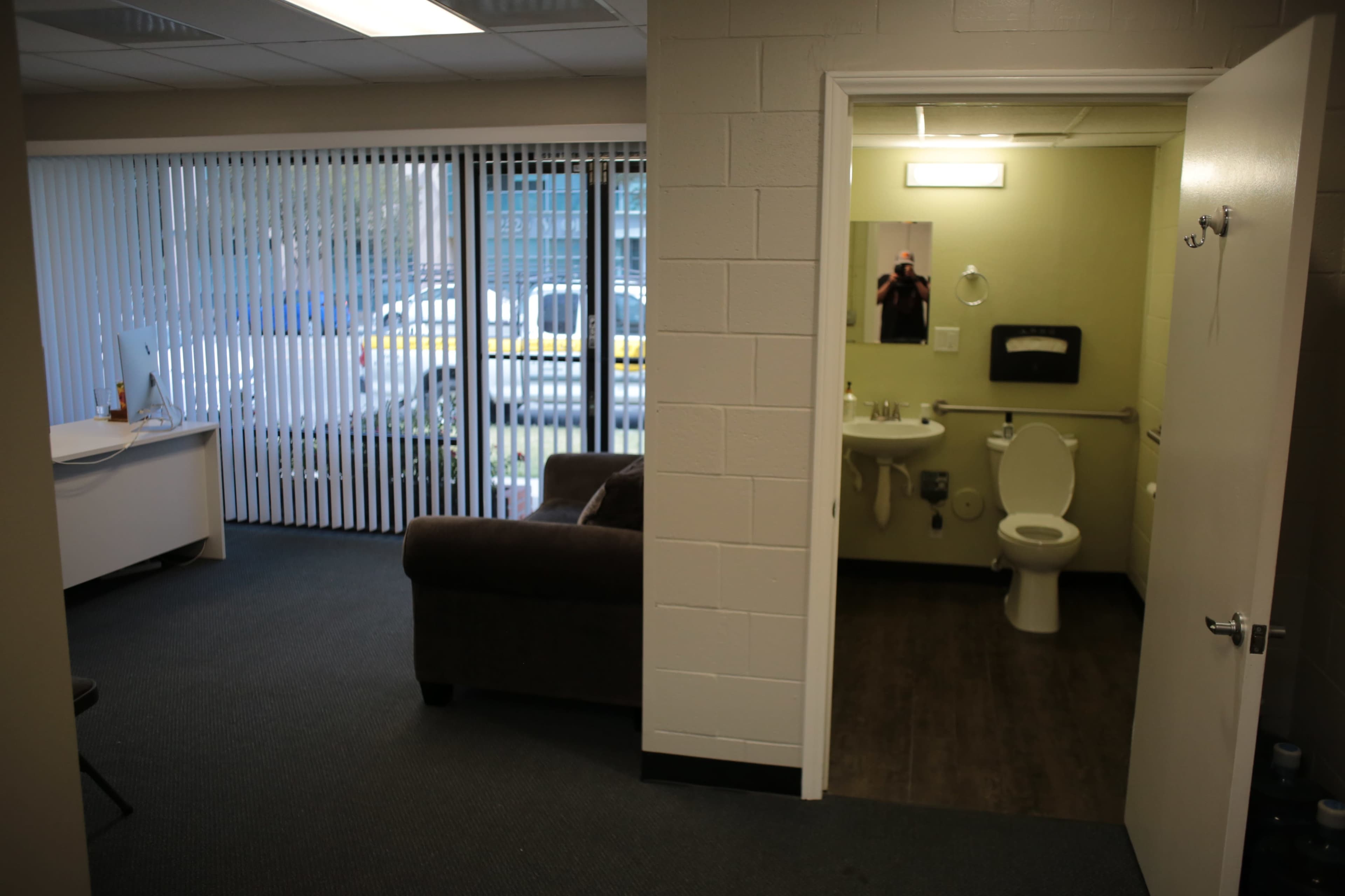 A small office space with a couch on the left and a bathroom visible through an open door on the right.