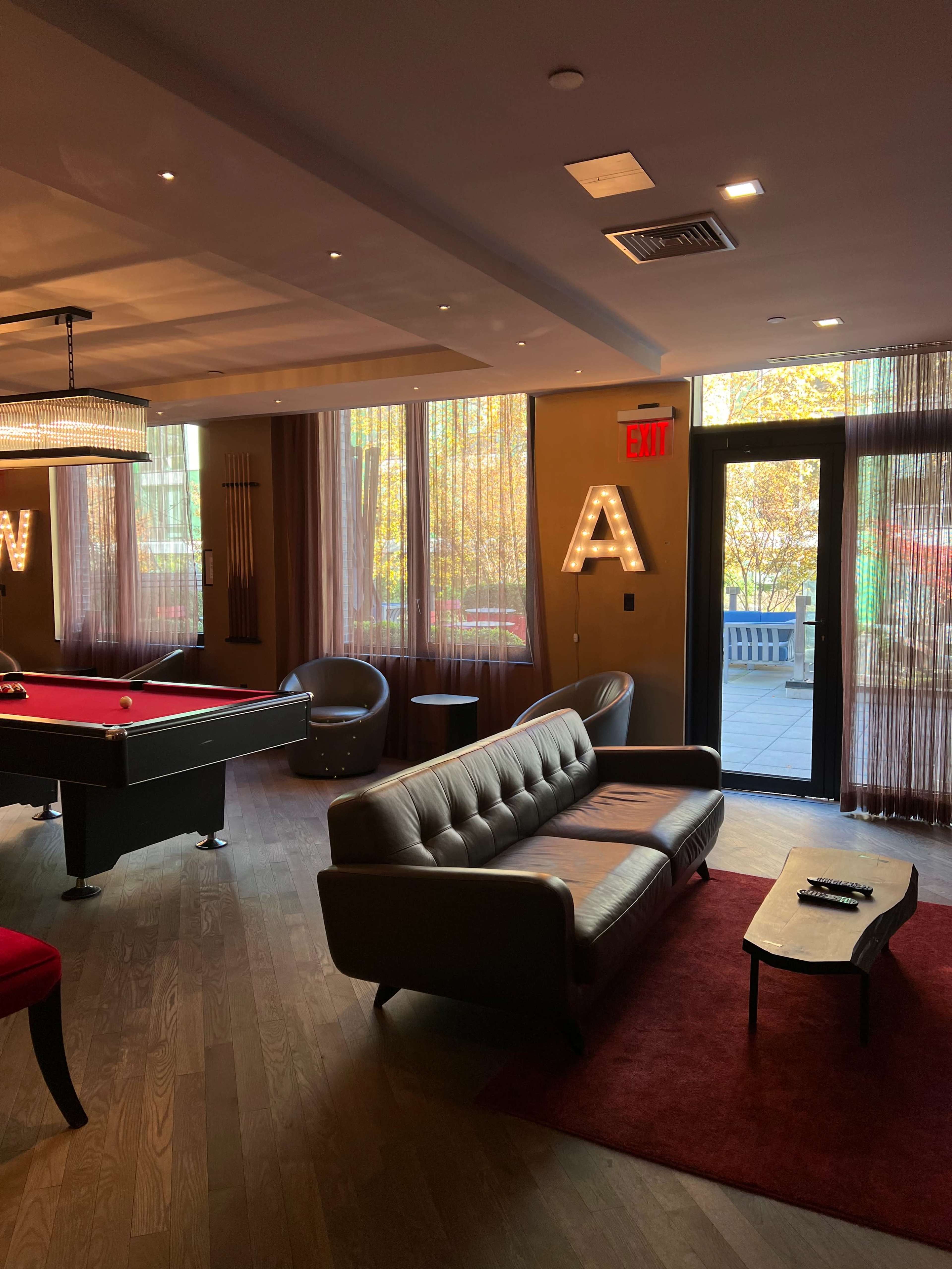 The interior features a pool table, a sofa, and large windows with visible autumn foliage outside.