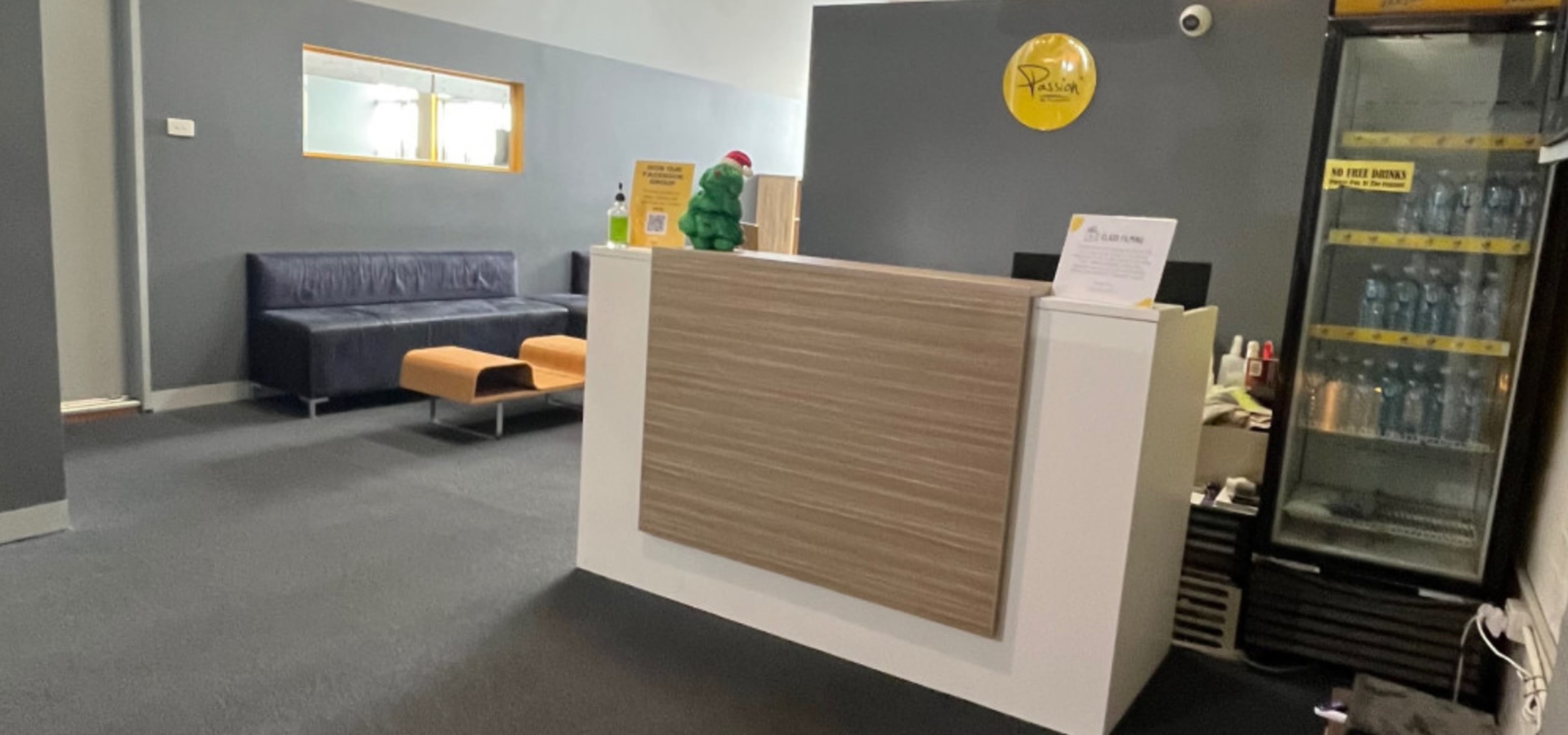 A reception area with a front desk, a dark sofa, and a fridge stocked with bottled drinks.