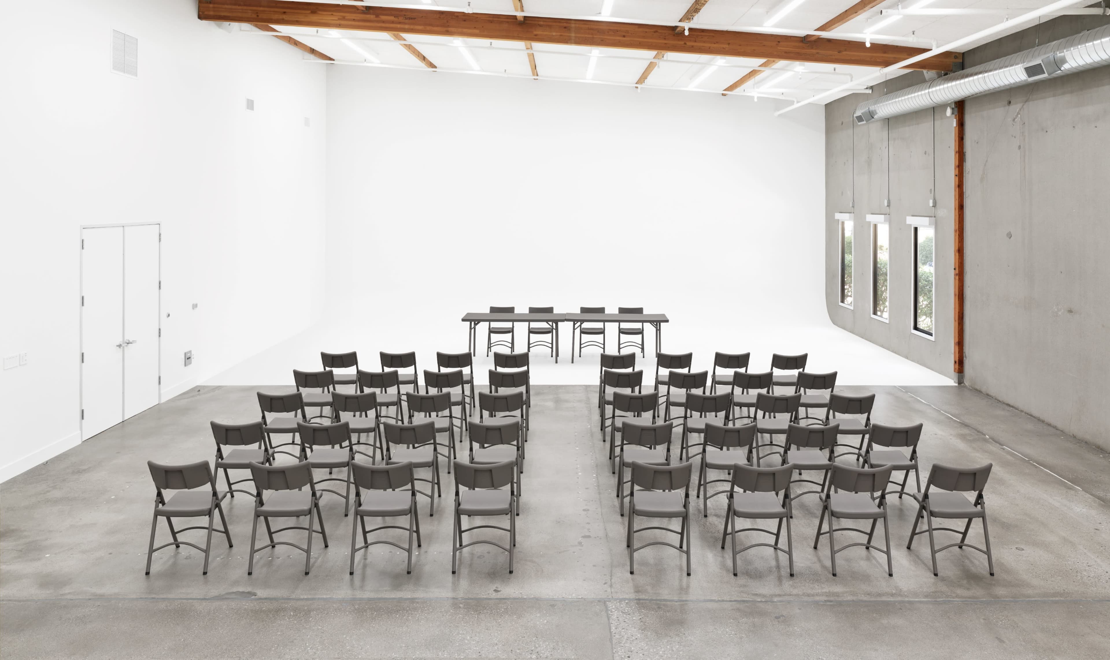 A spacious room features a rectangular table at the front, facing rows of gray chairs arranged in a symmetrical layout.