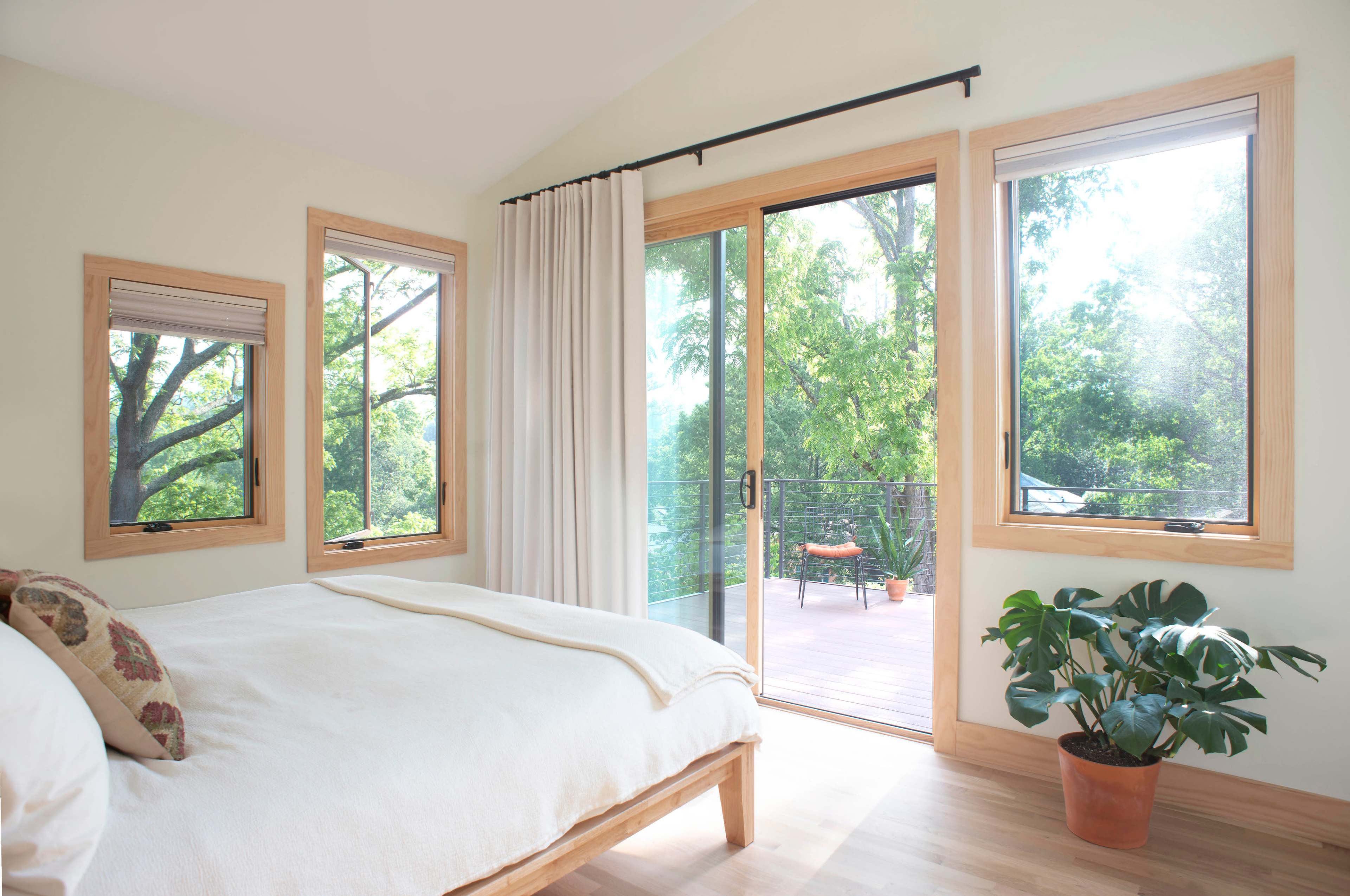 A bright bedroom features a bed positioned beside large windows that open to a deck with outdoor seating.