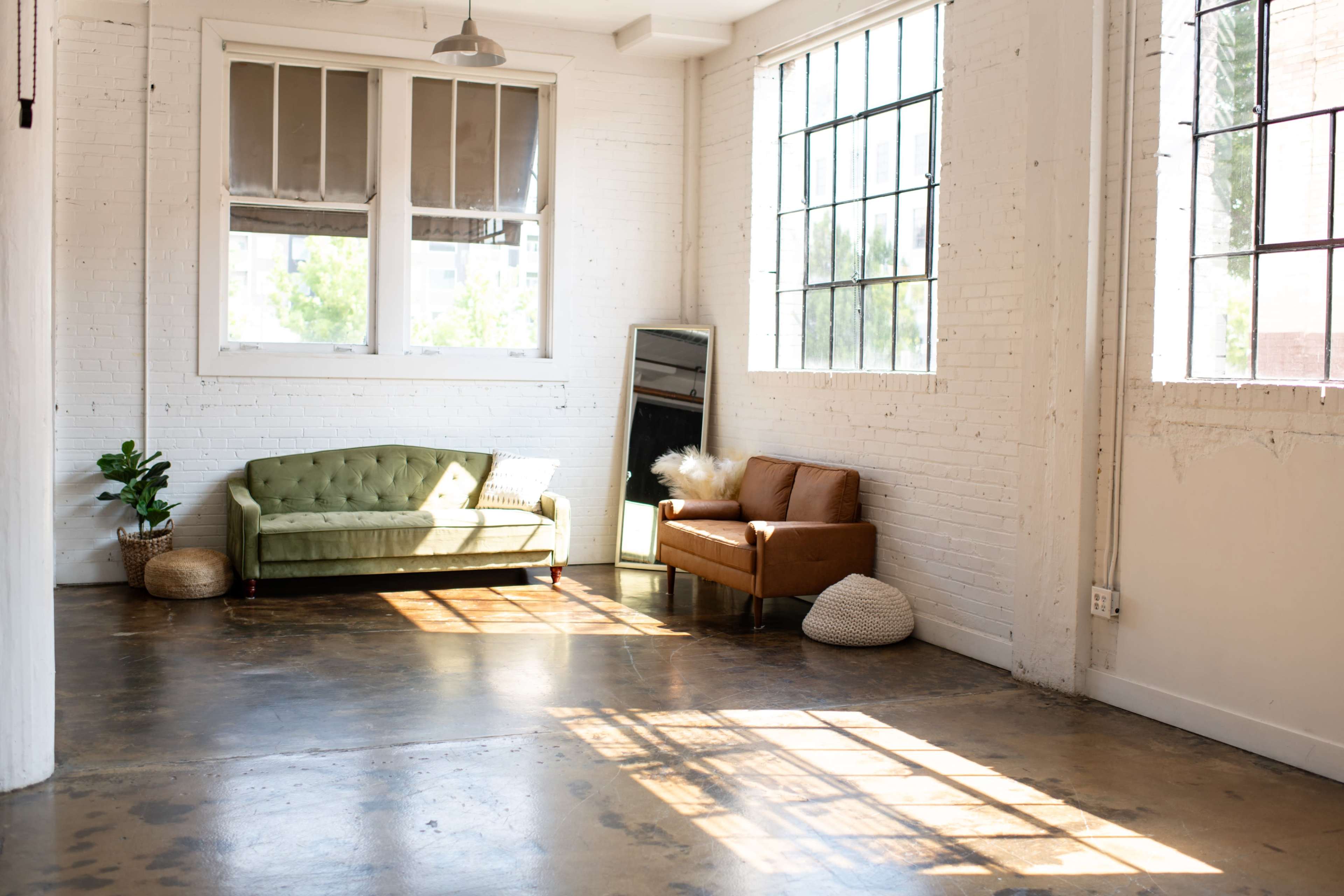 A bright, minimalistic room with two couches, a large mirror, and sunlight casting shadows on the polished concrete floor.