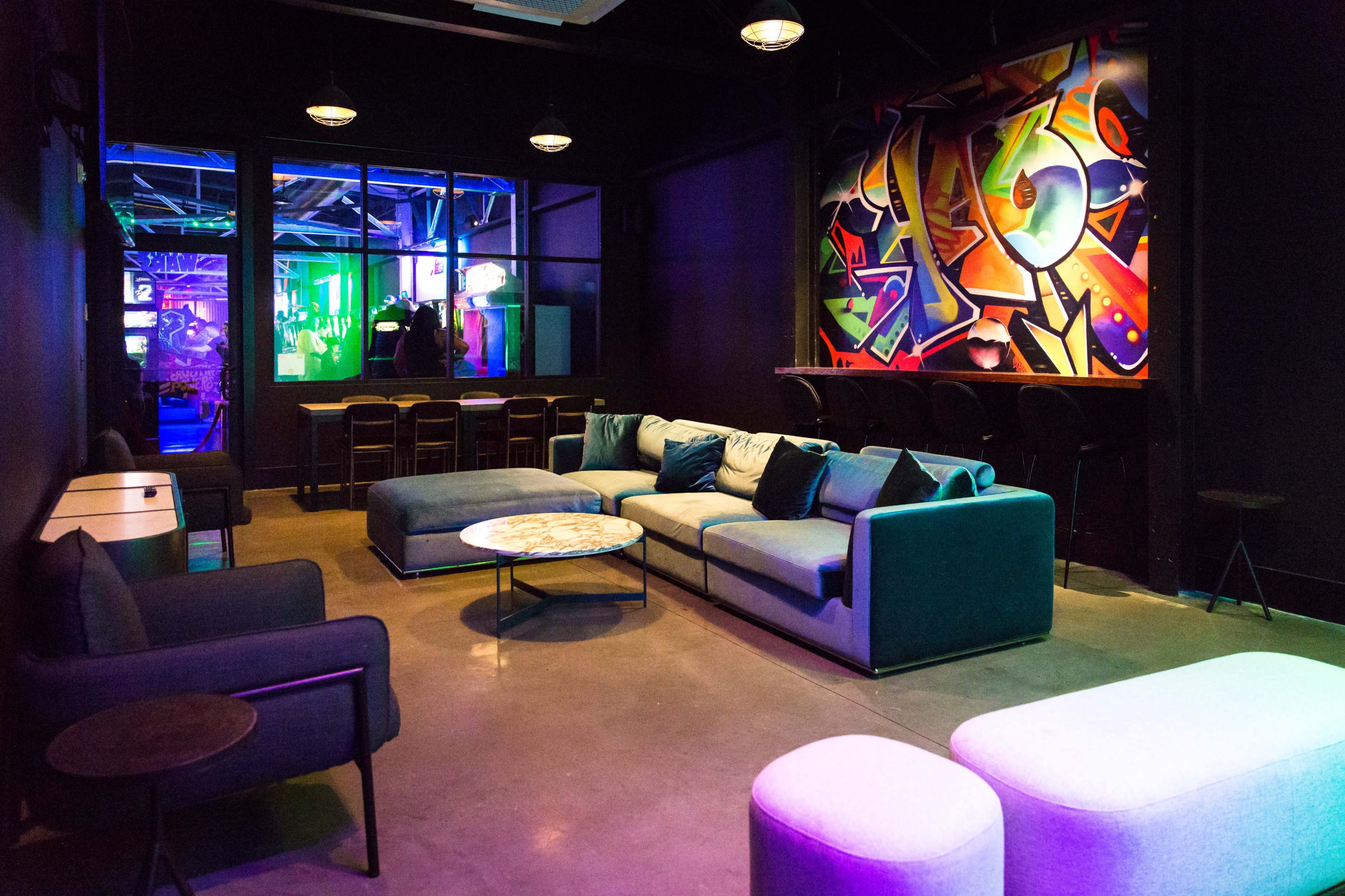 A lounge area features a modern seating arrangement with a large sofa and a coffee table, complemented by colorful graffiti art on the wall and ambient lighting.