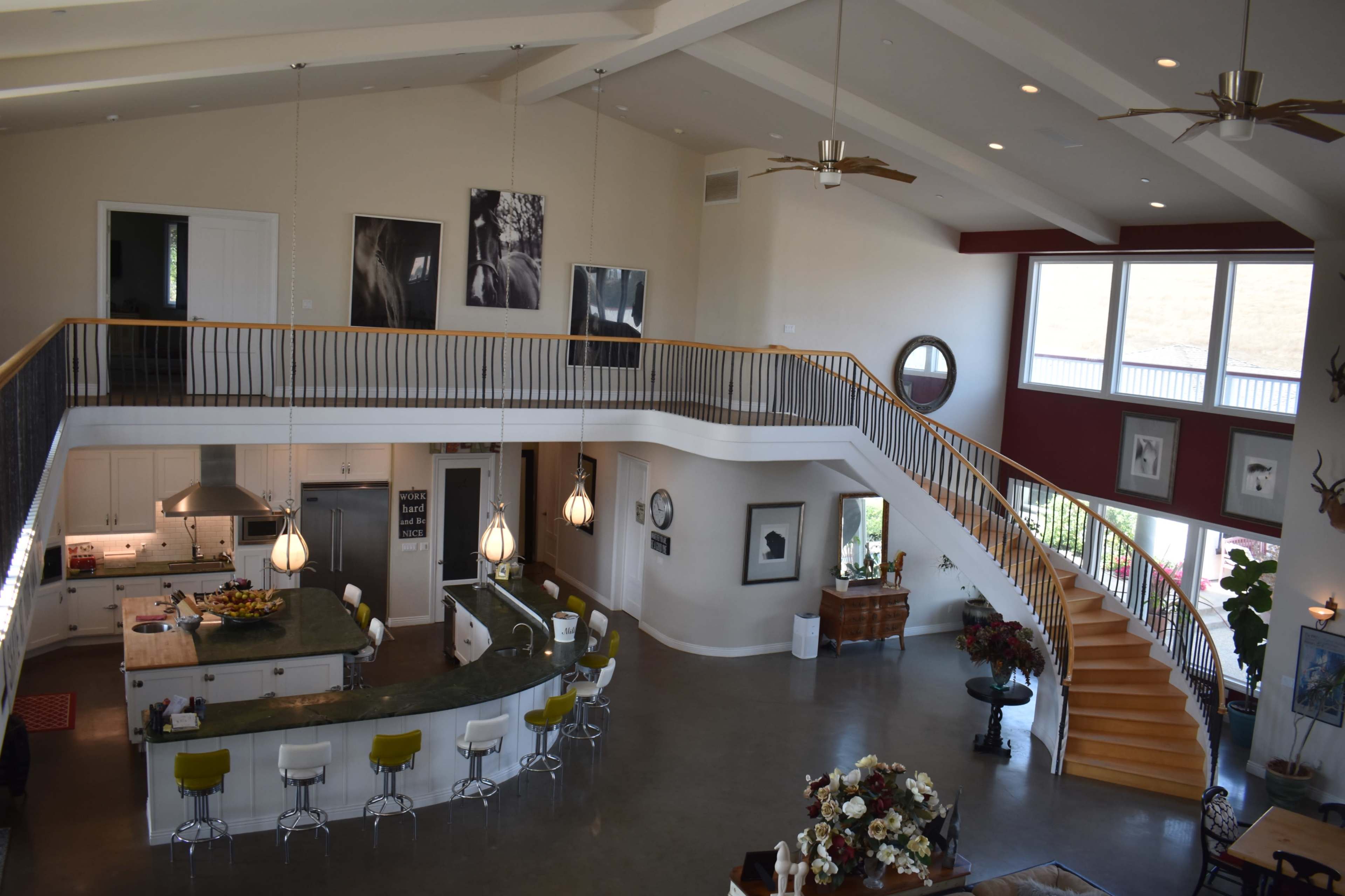 The image shows a spacious open-concept living area with a large kitchen island, a sweeping staircase, and large windows that allow natural light to fill the space.