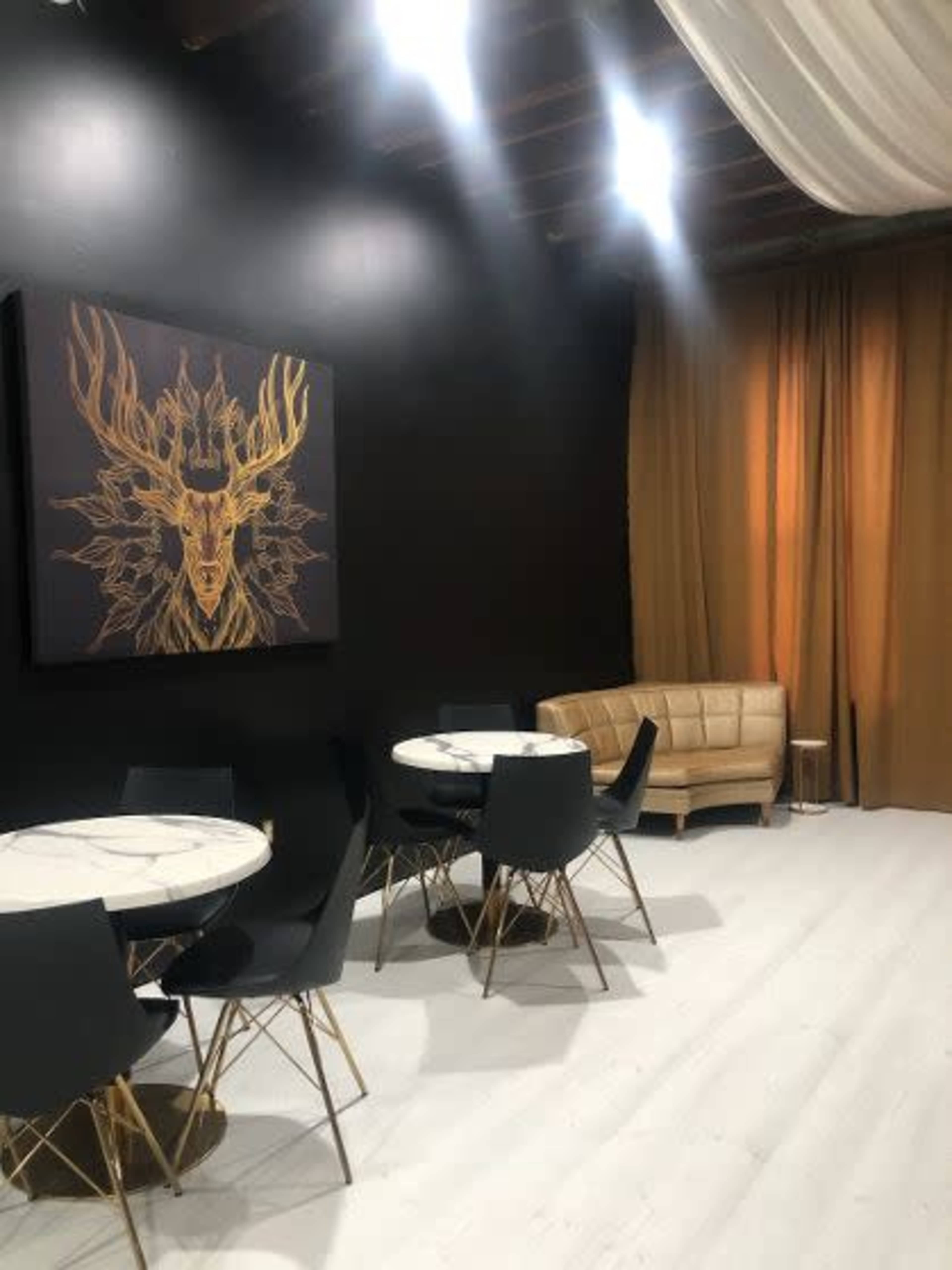 A modern interior space with black walls, a large deer artwork, a beige couch, and several round tables with black chairs.