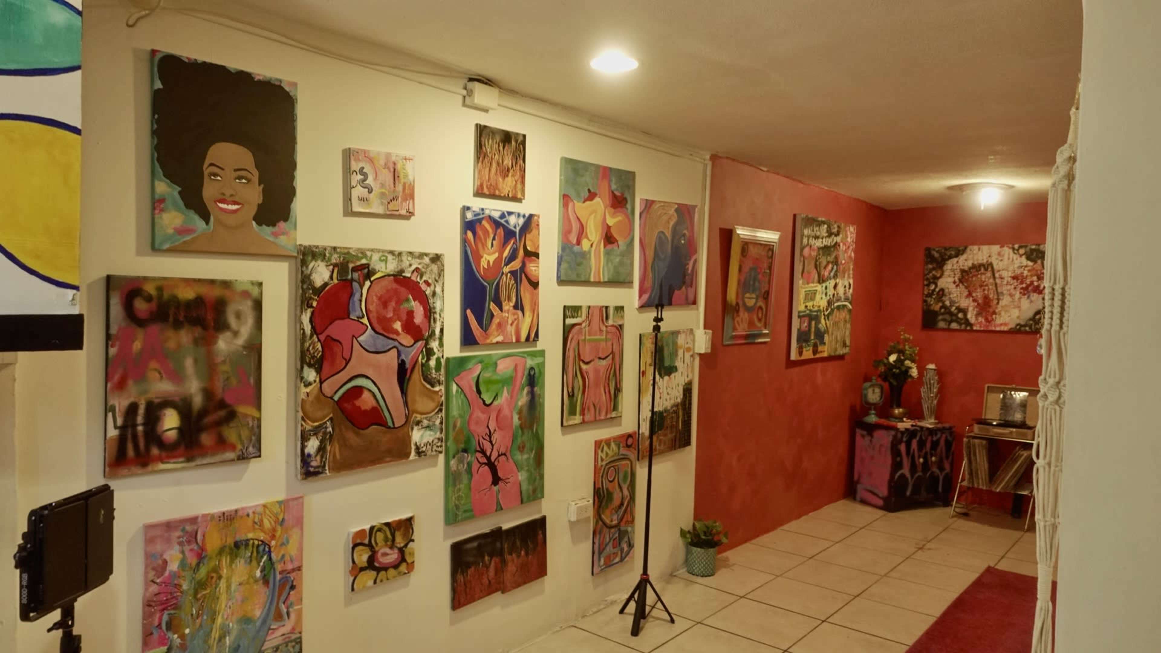 A hallway adorned with various colorful paintings on the walls, leading to a red-painted room at the end.
