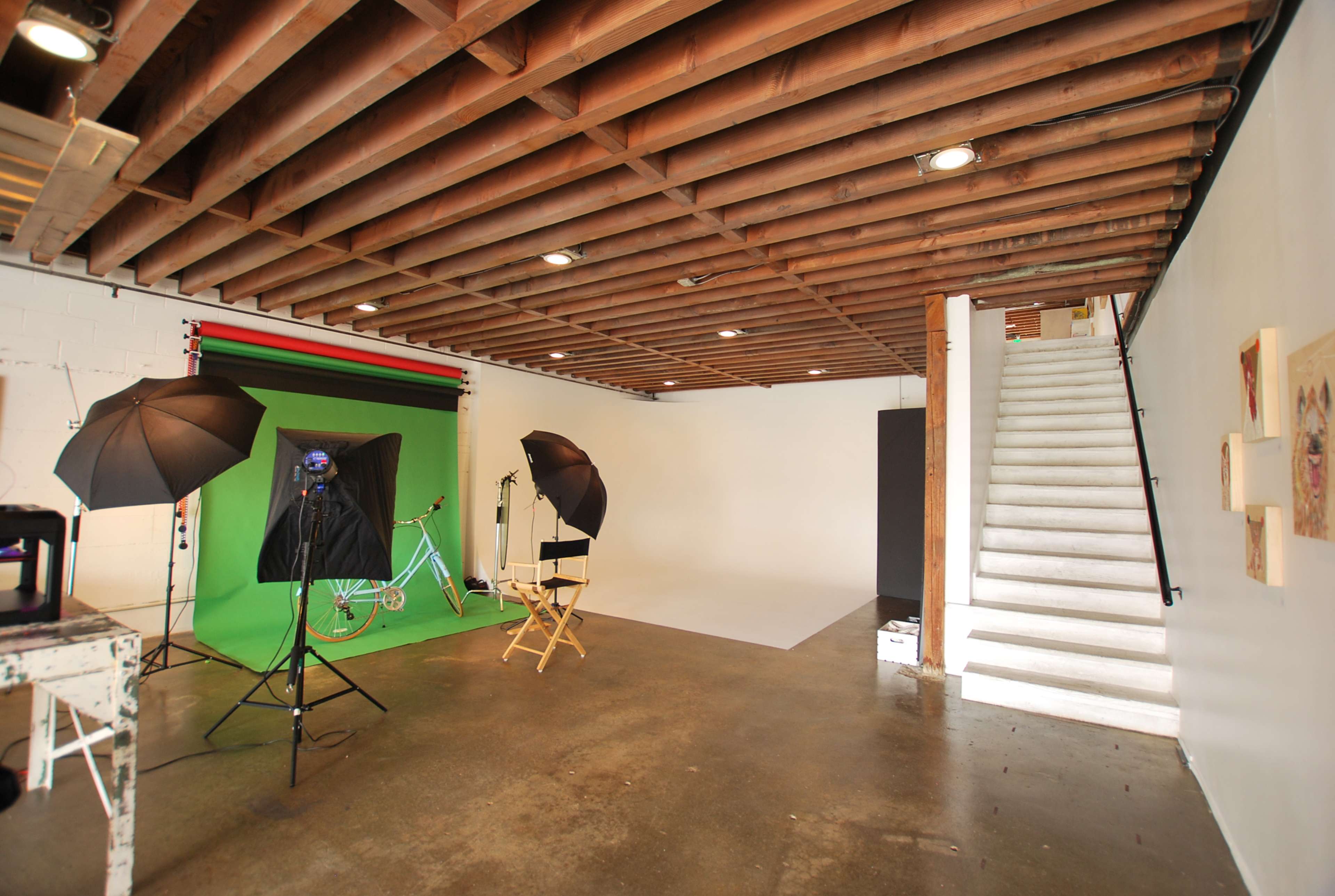 The image shows a photography studio with a backdrop setup, lighting equipment, and a staircase leading to another level.