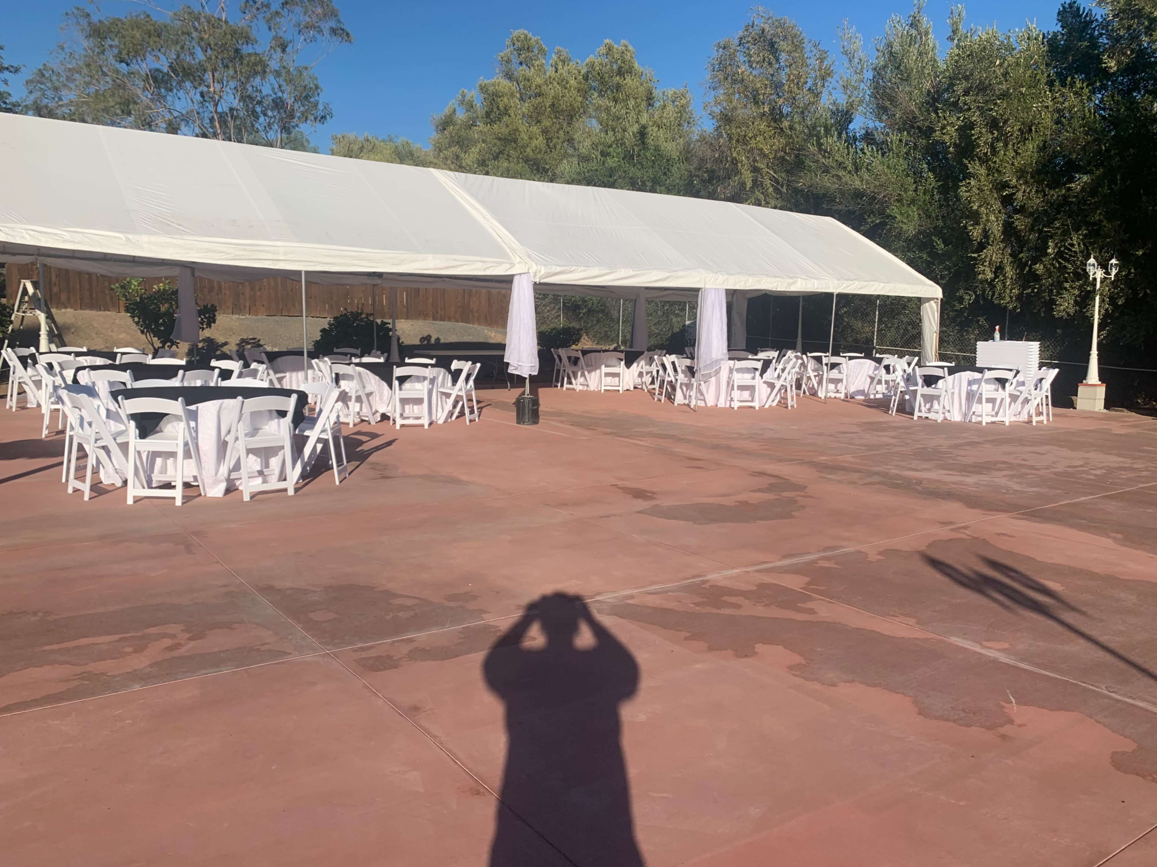 A large tent is set up over an outdoor area with white tables and chairs arranged for an event.