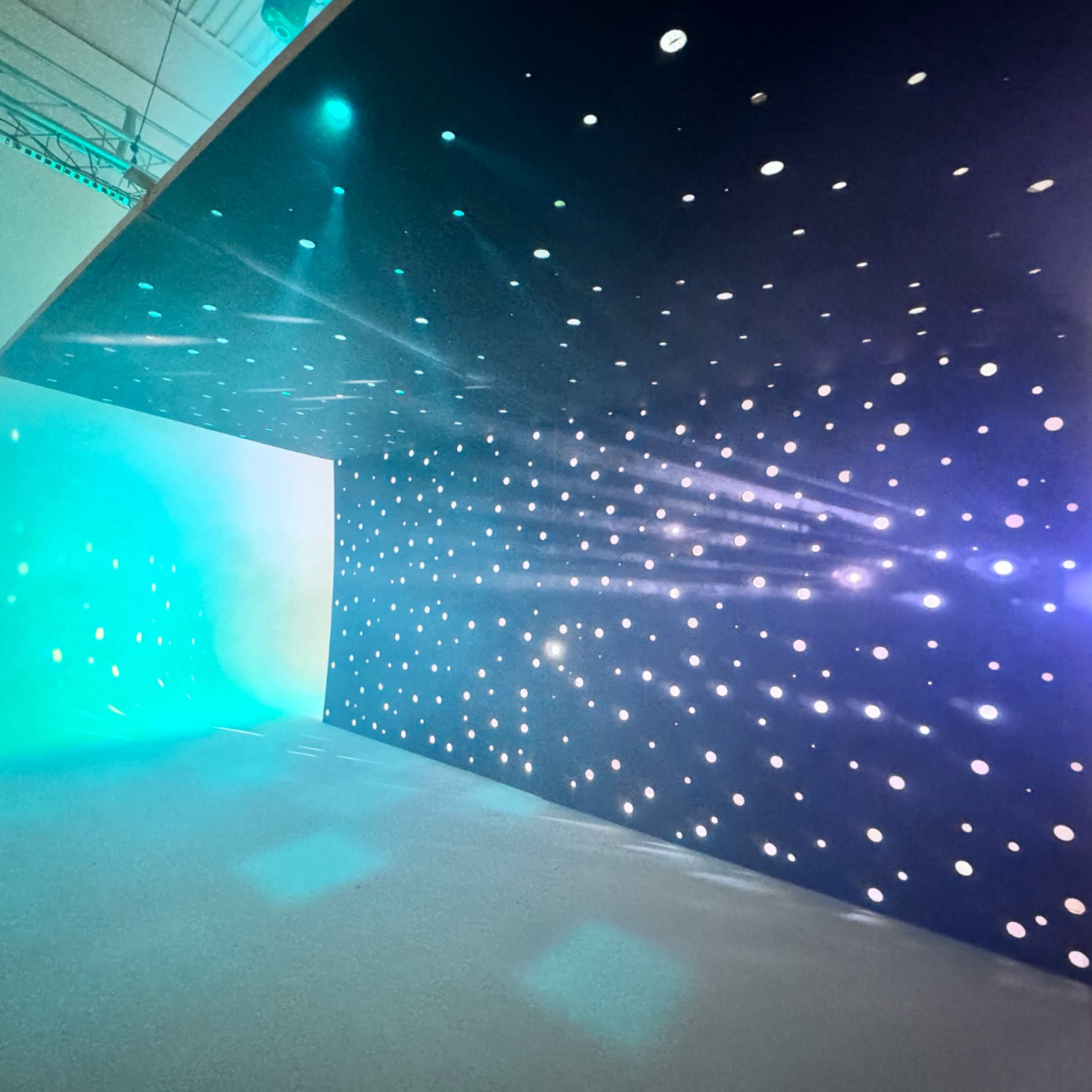 A room with a dark ceiling and wall illuminated by scattered lights, creating a starry effect.