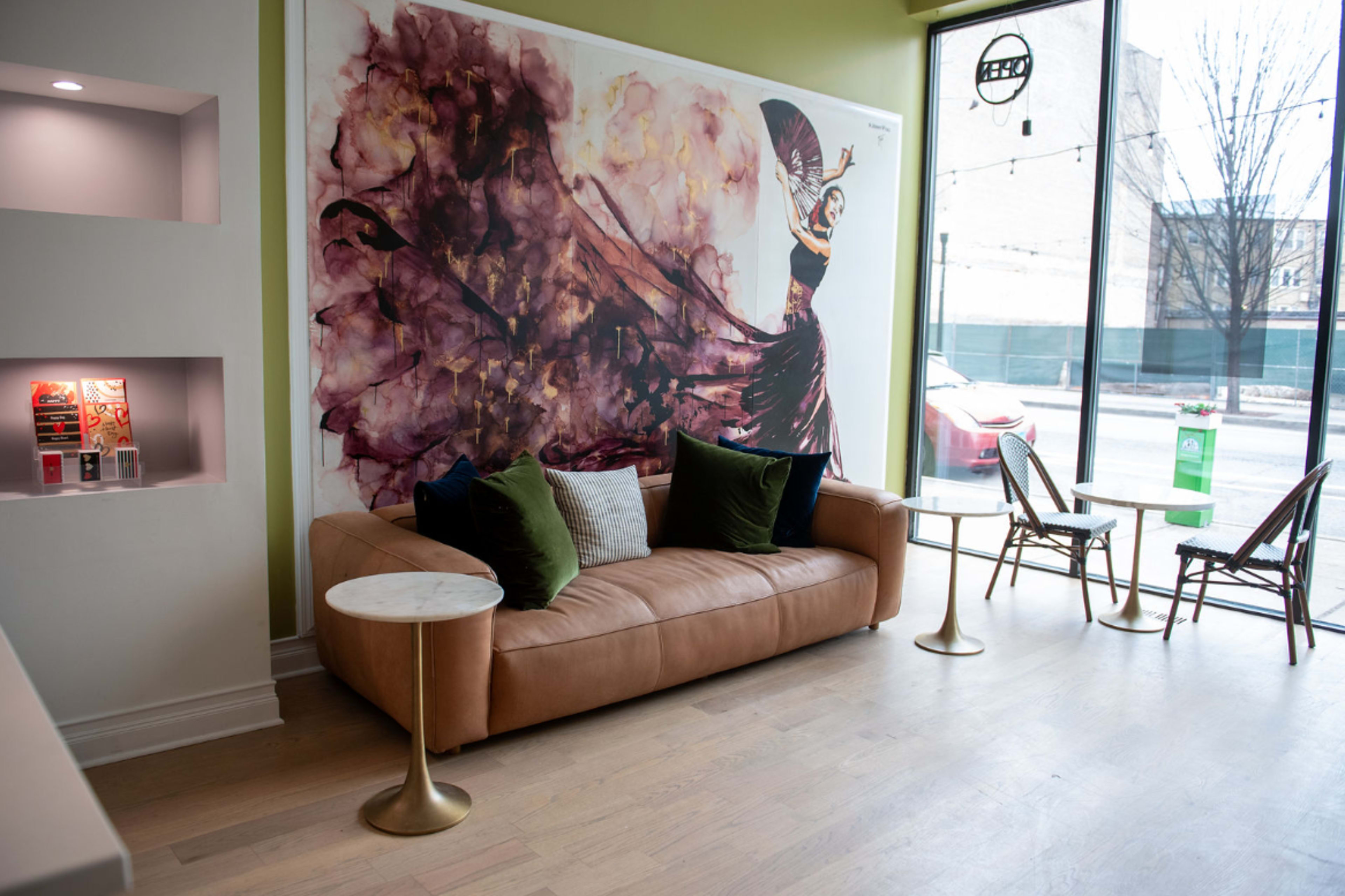 The scene features a leather sofa with decorative pillows in front of a large mural depicting a dancer, beside glass tables in a modern interior space.