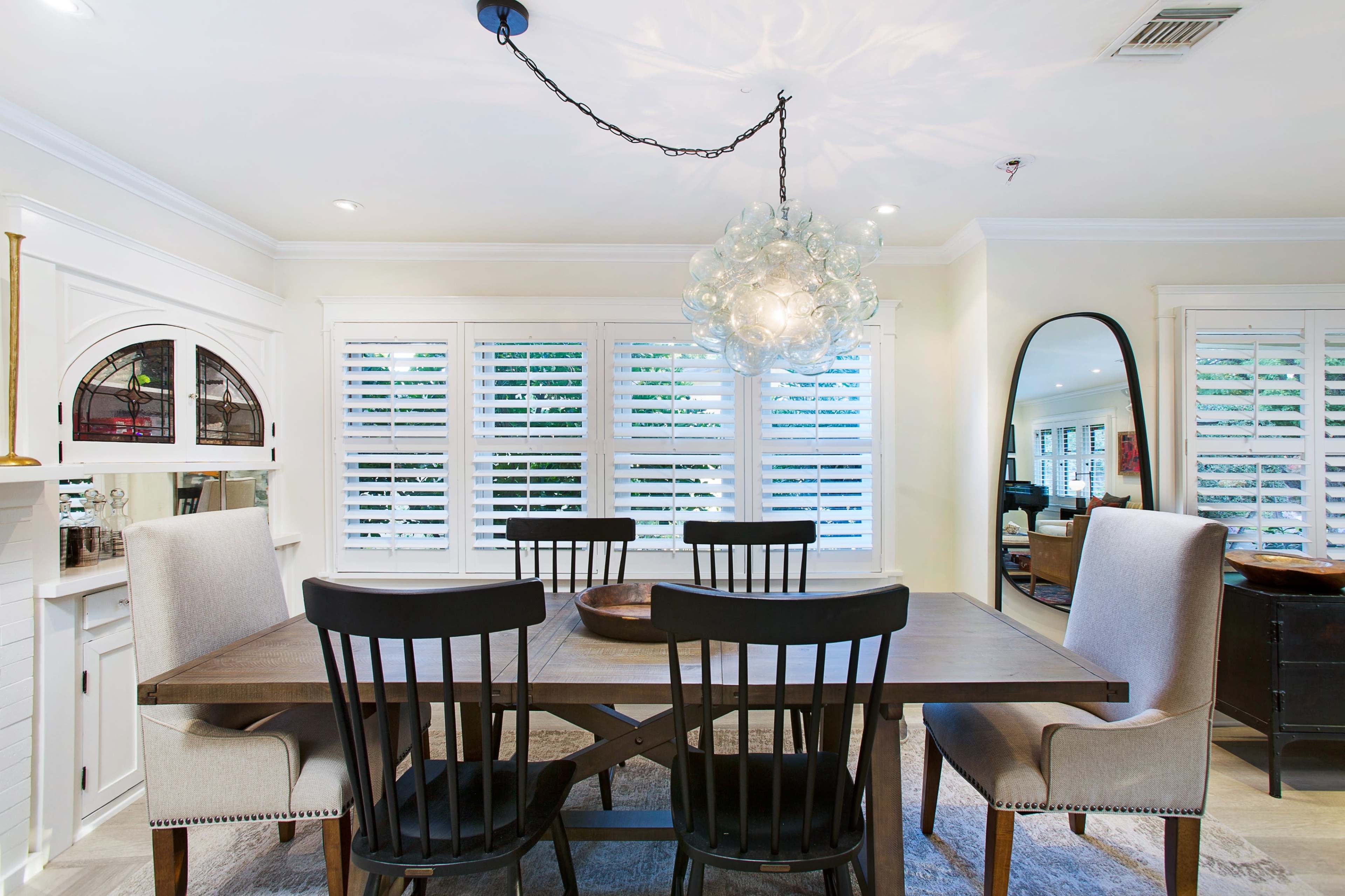 A modern dining room features a wooden table surrounded by four black chairs and two upholstered beige chairs, with a decorative chandelier hanging above.