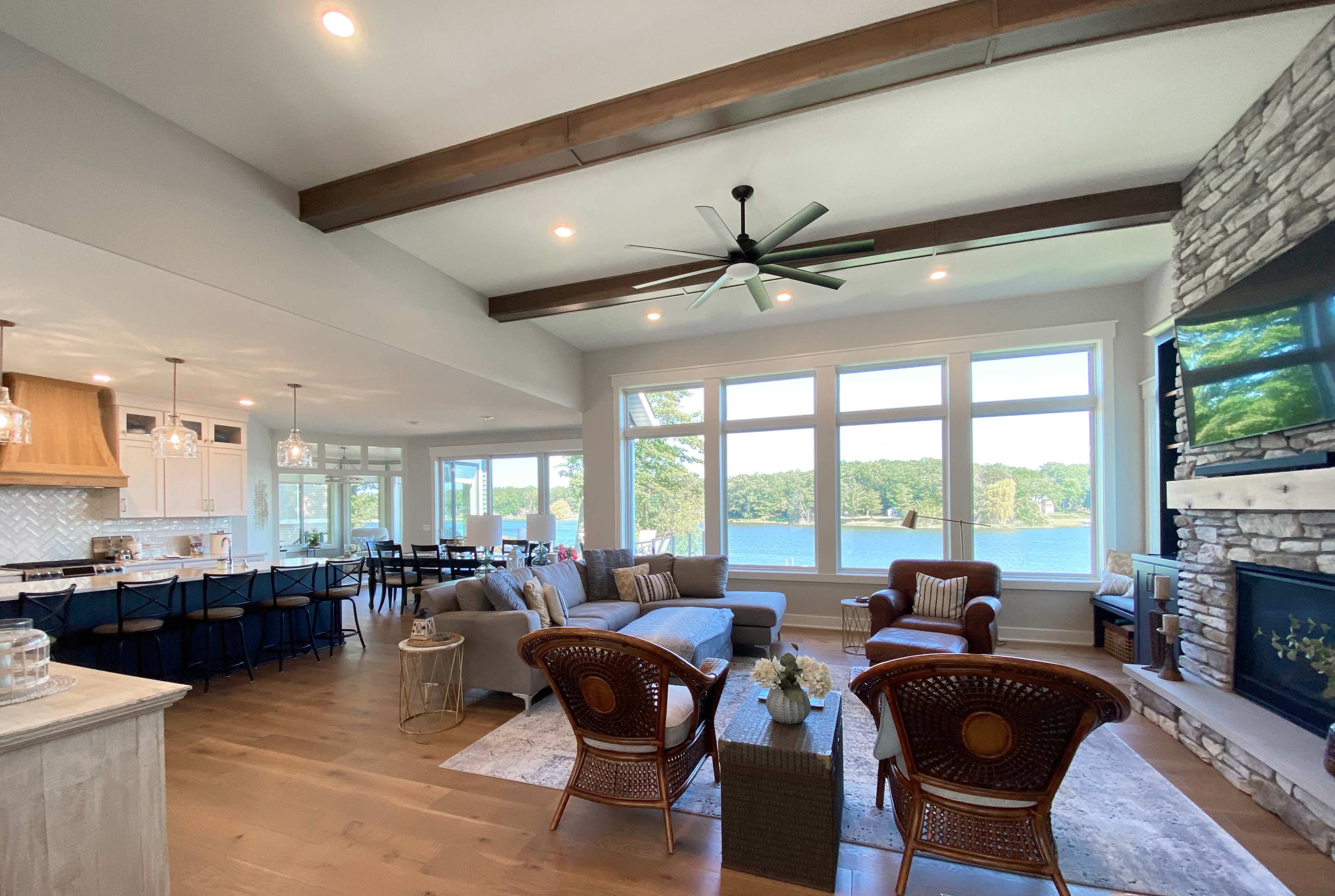 A modern living room with a view of a lake, featuring a combination of a sofa, chairs, and a stone fireplace.