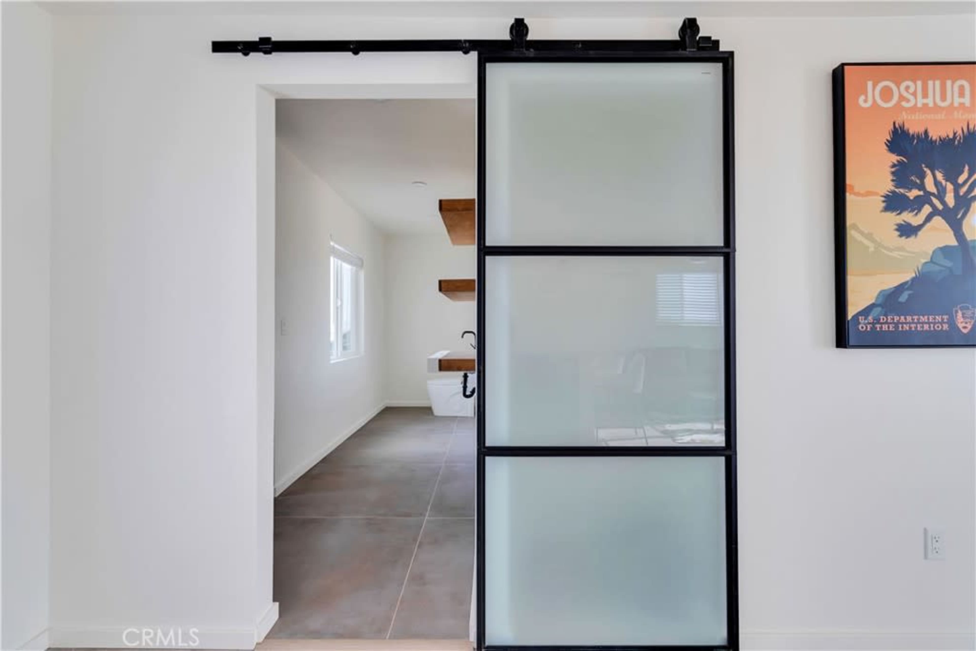 A sliding glass door framed in black, leading to a room with white walls and a wooden shelf.