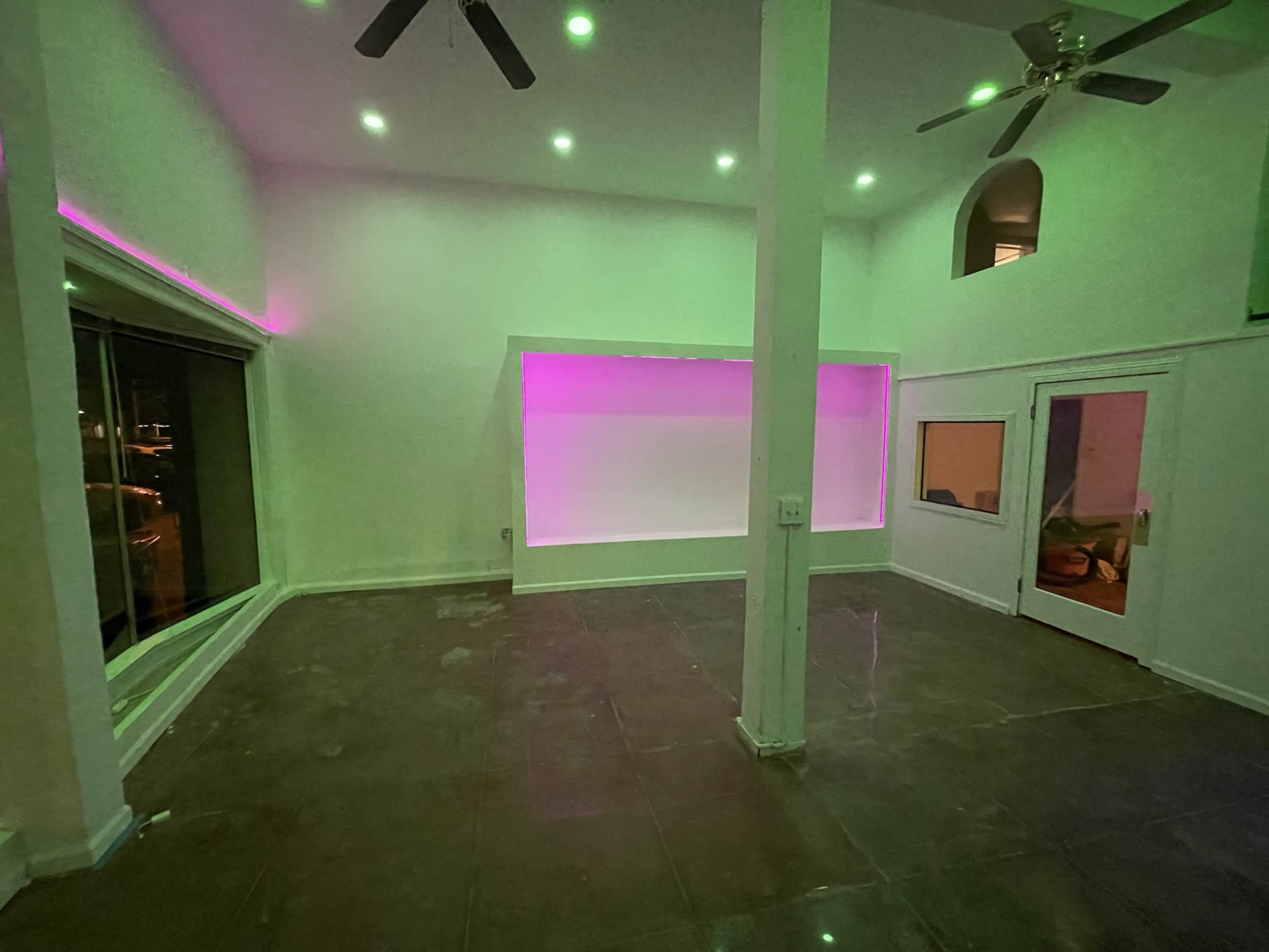 A spacious room with a high ceiling, featuring pink backlighting along one wall and large windows.