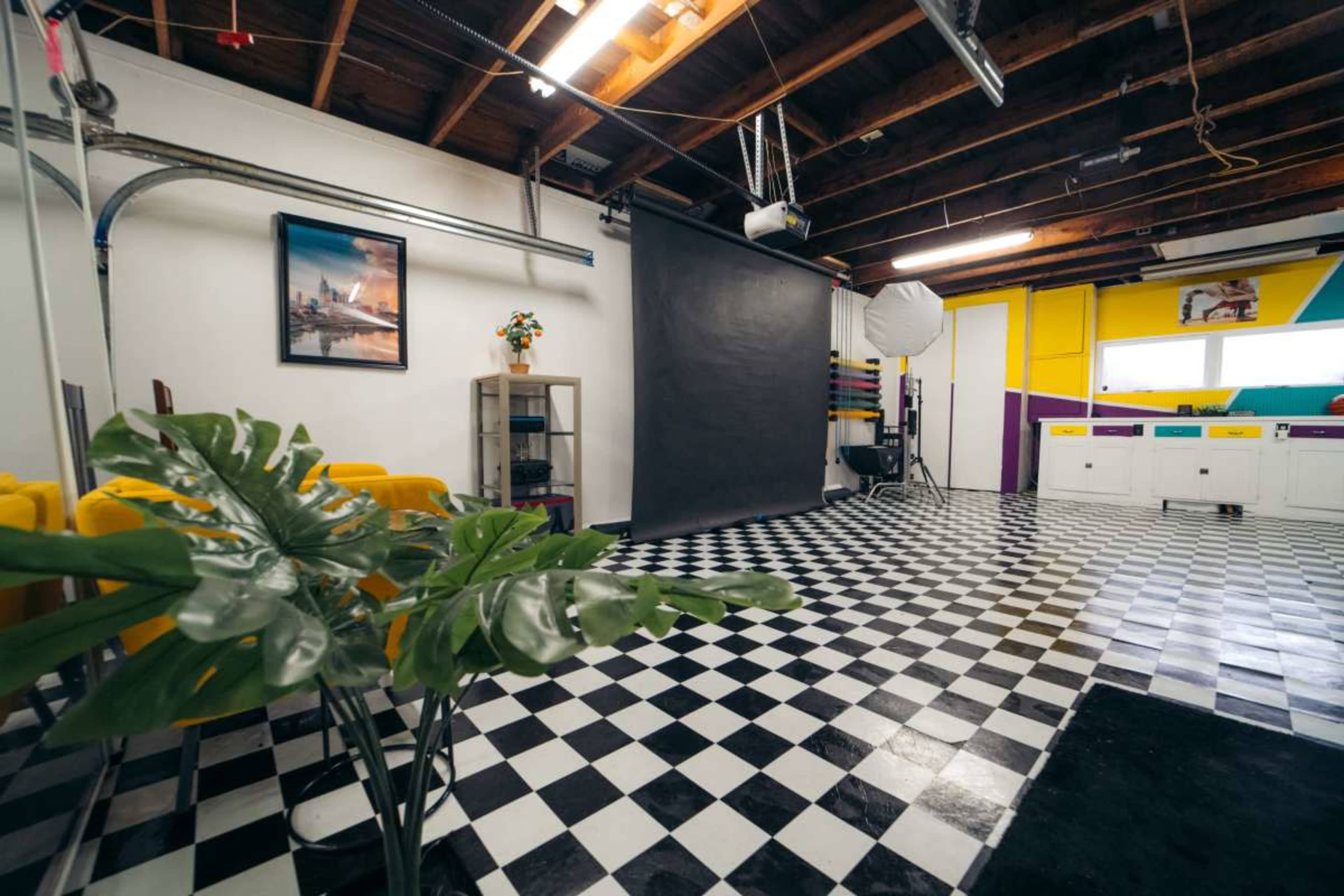A spacious studio with a checkered black-and-white floor, a dark backdrop, colorful walls, and a few studio equipment elements.