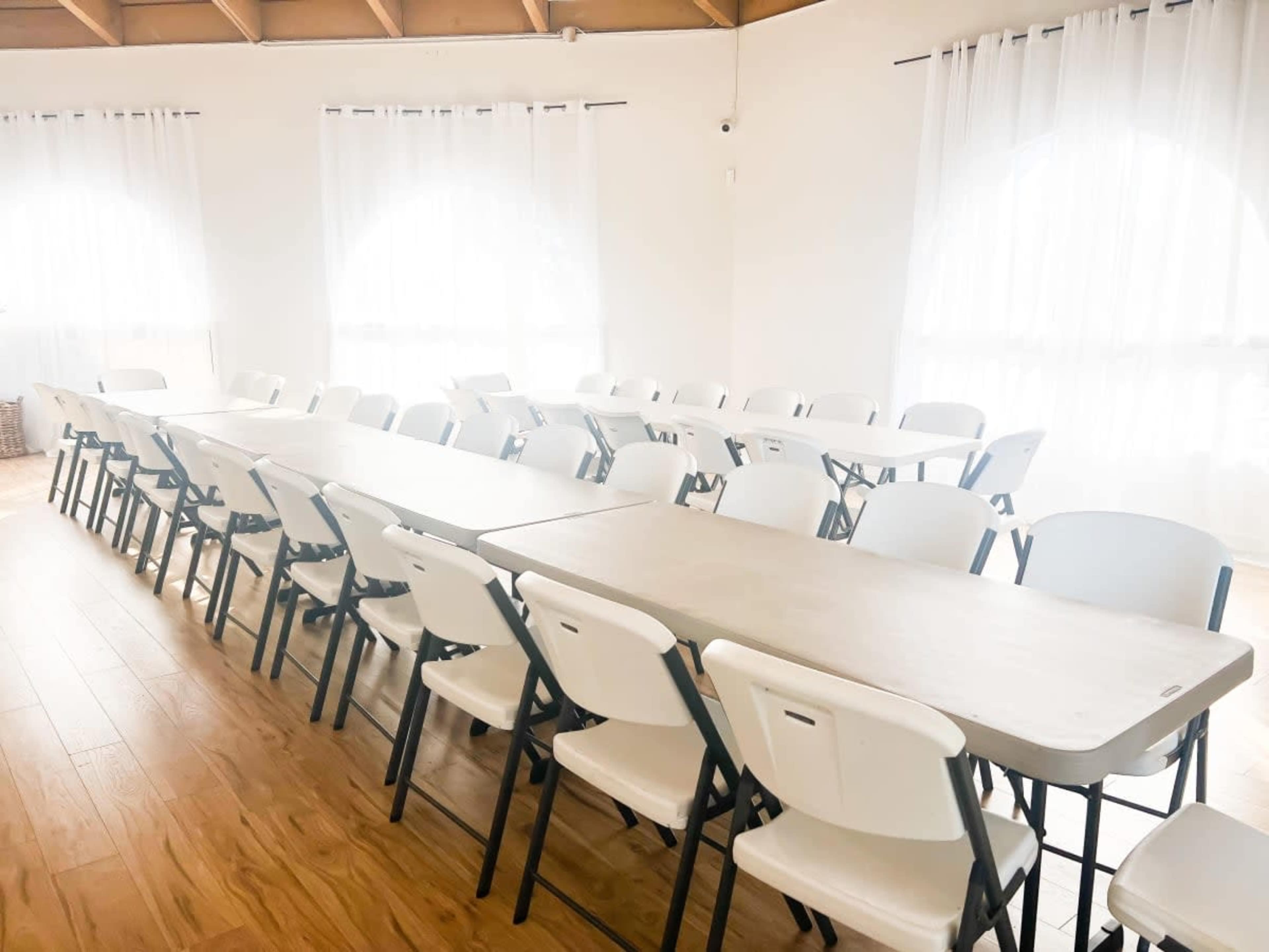 A spacious room features several rows of long tables with white folding chairs arranged neatly around them.