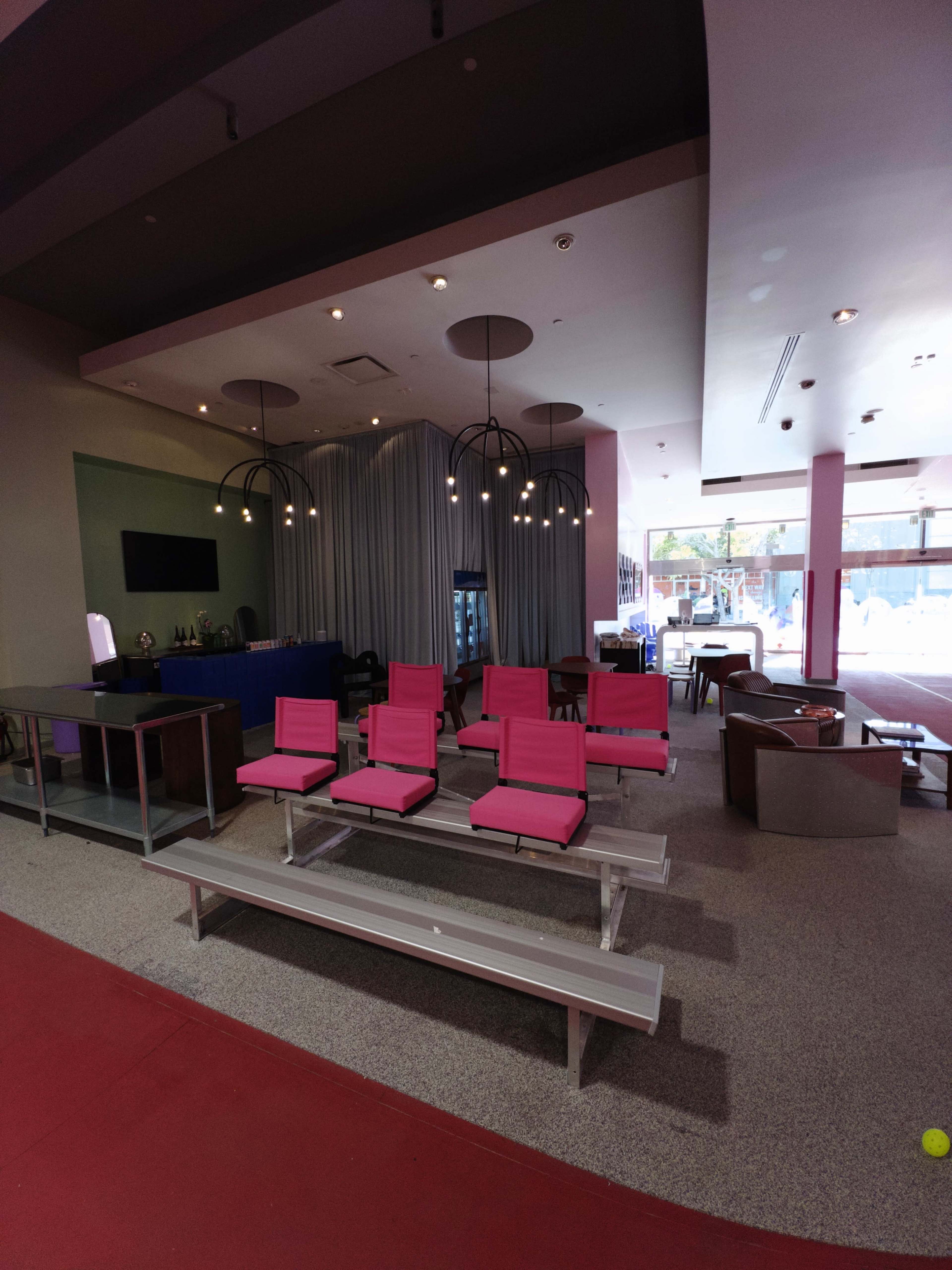 A modern indoor lounge area featuring pink chairs, gray benches, and a reception desk with decorative lighting in the background.