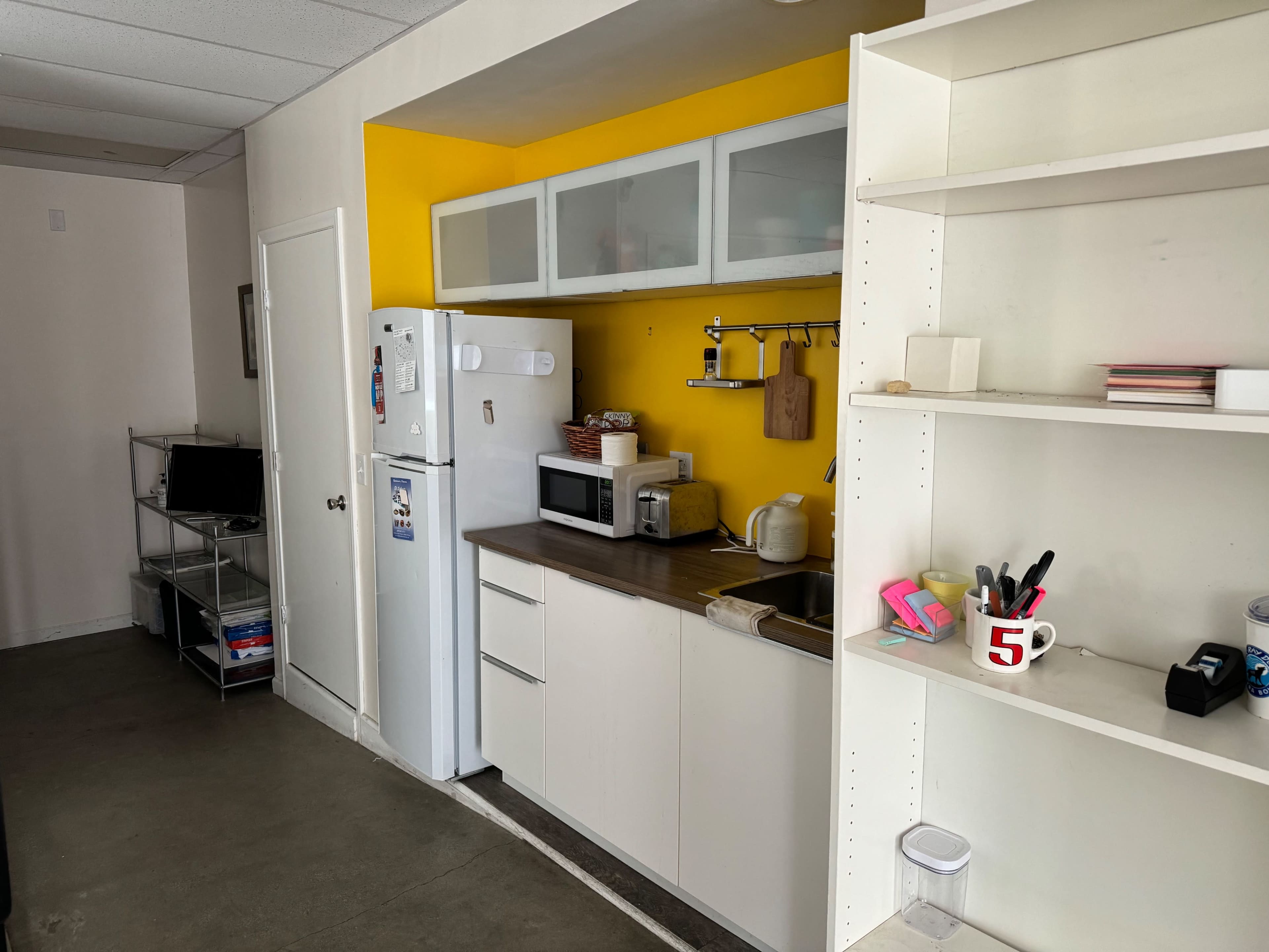 A compact kitchen area with yellow walls, a white refrigerator, a microwave, and open shelving.
