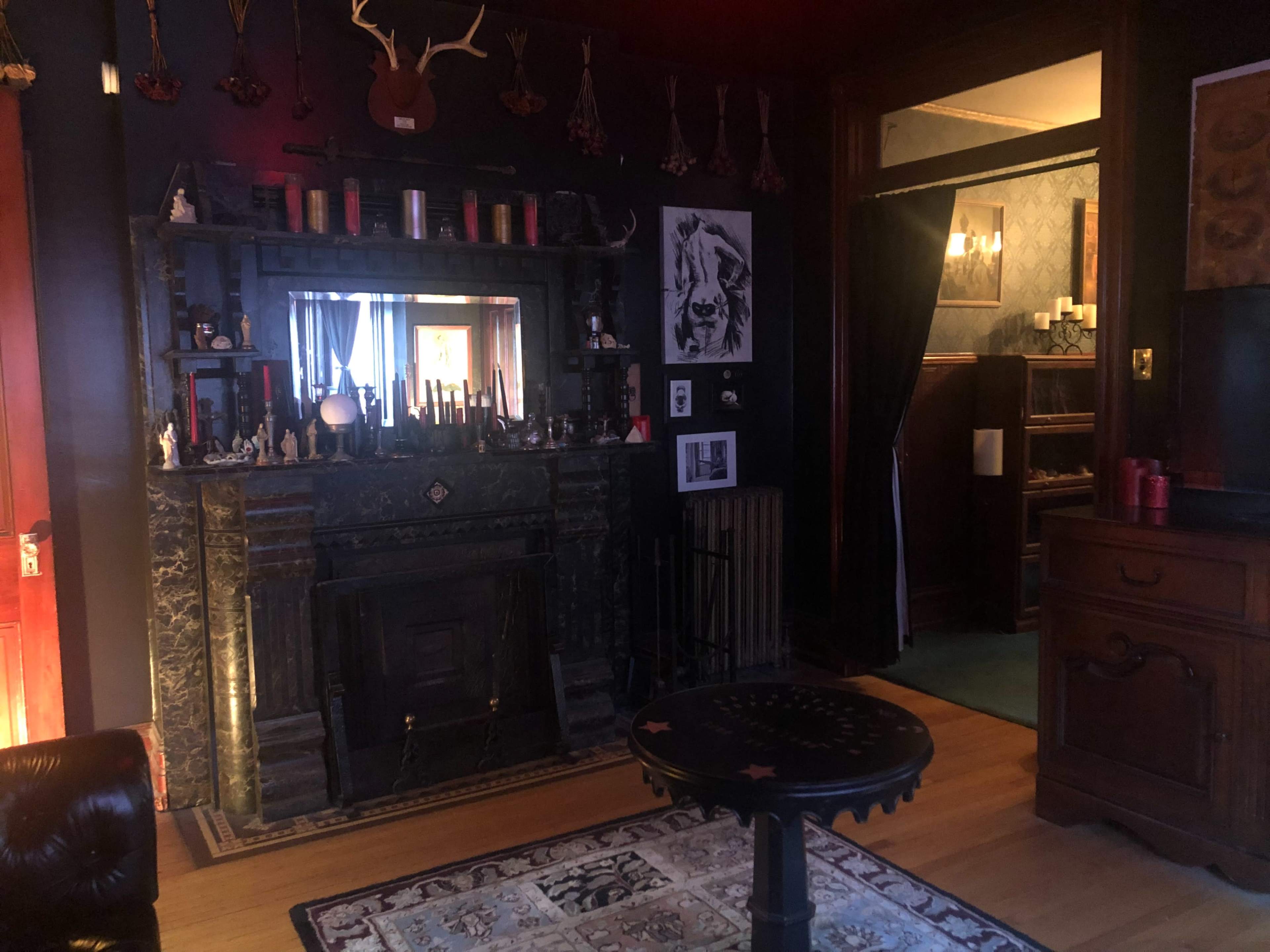 A dimly lit room featuring a dark fireplace with ornate detailing, surrounded by various decorations and a visible doorway leading to another space.