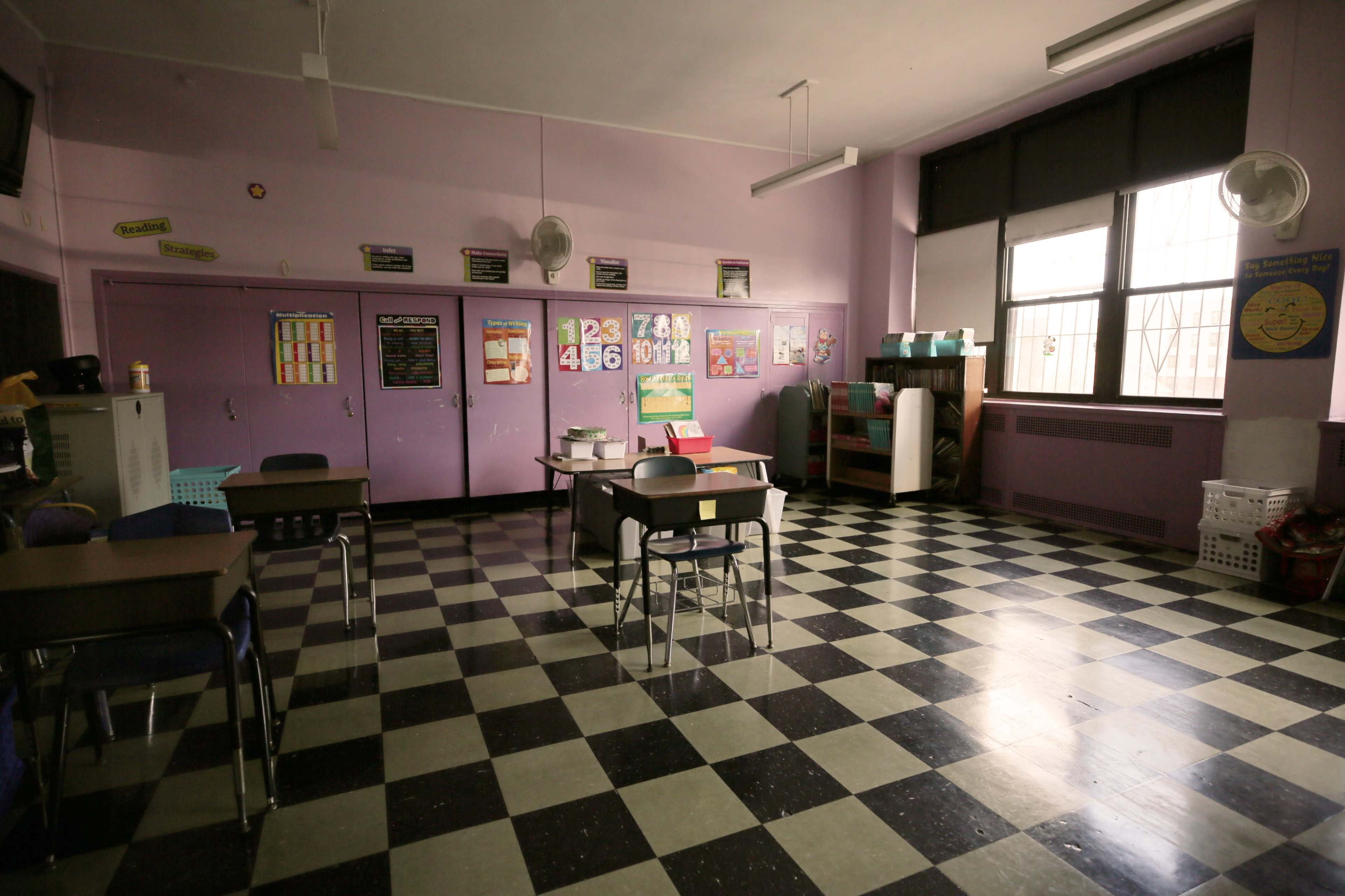 An empty classroom features purple walls, a checkered floor, and organized desks with educational materials on the walls.
