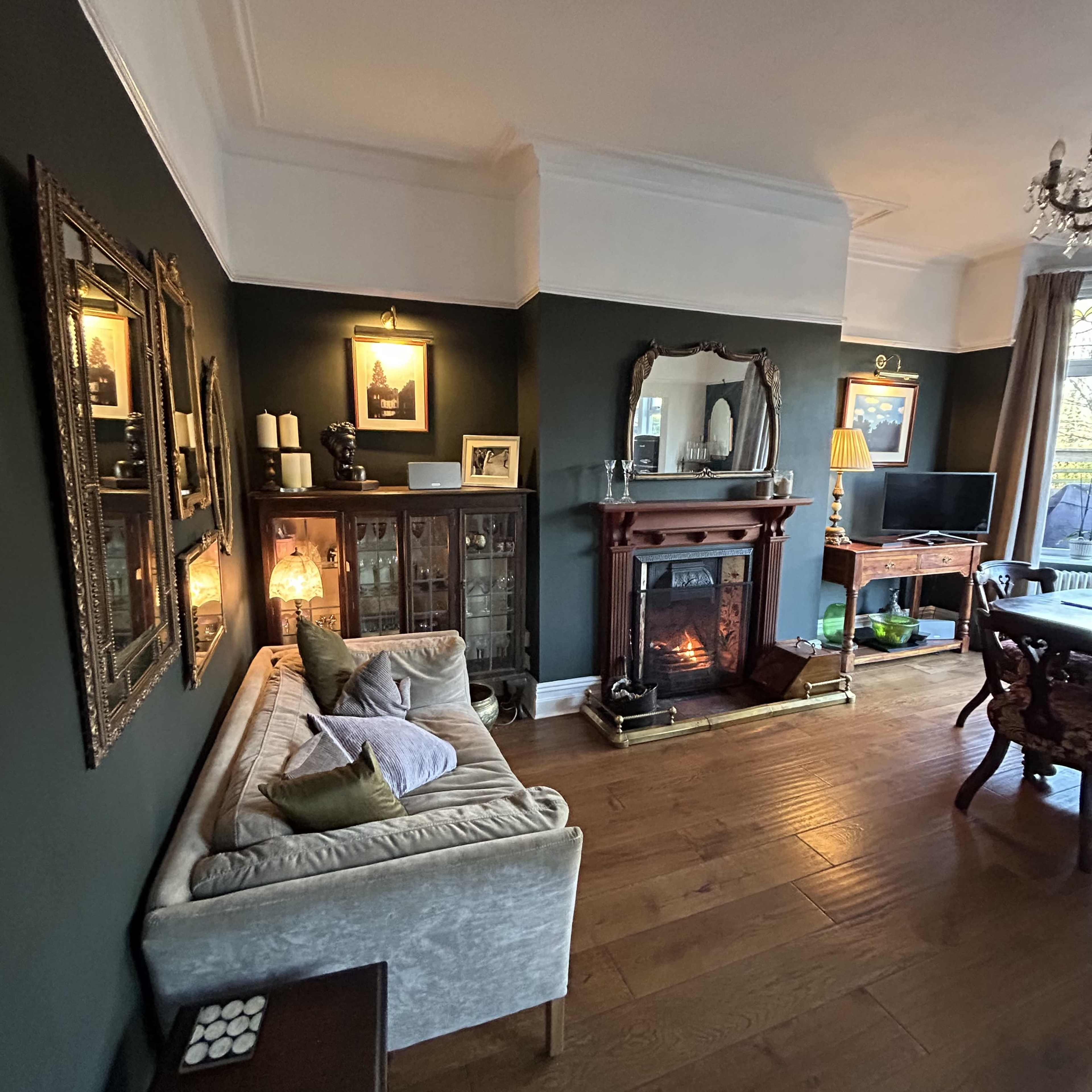 The image shows a cozy living room featuring a fireplace, a sofa with decorative pillows, a wooden cabinet, and framed artwork on the walls.
