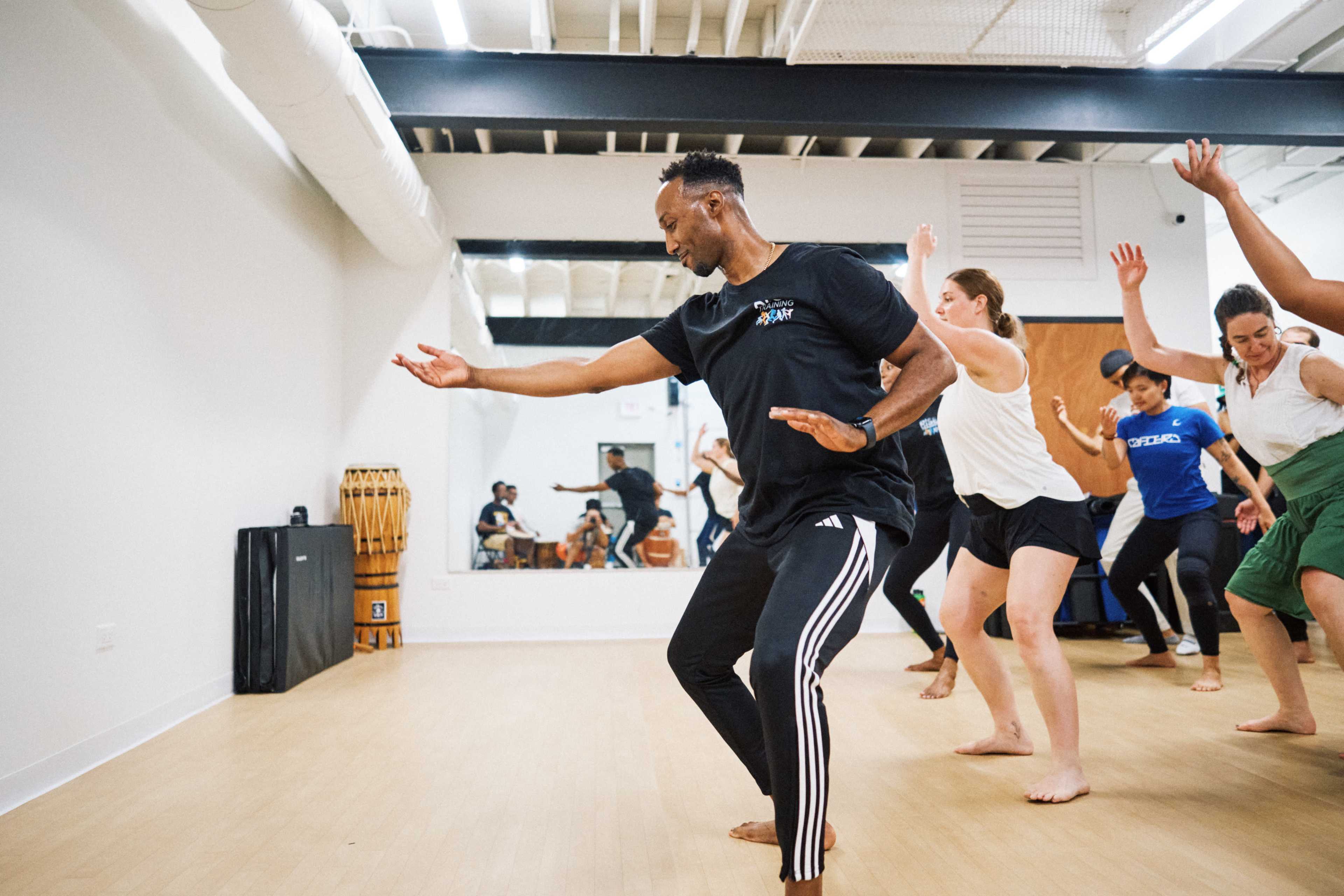 A group of people are participating in a dance class in a studio with mirrored walls and wooden floors.