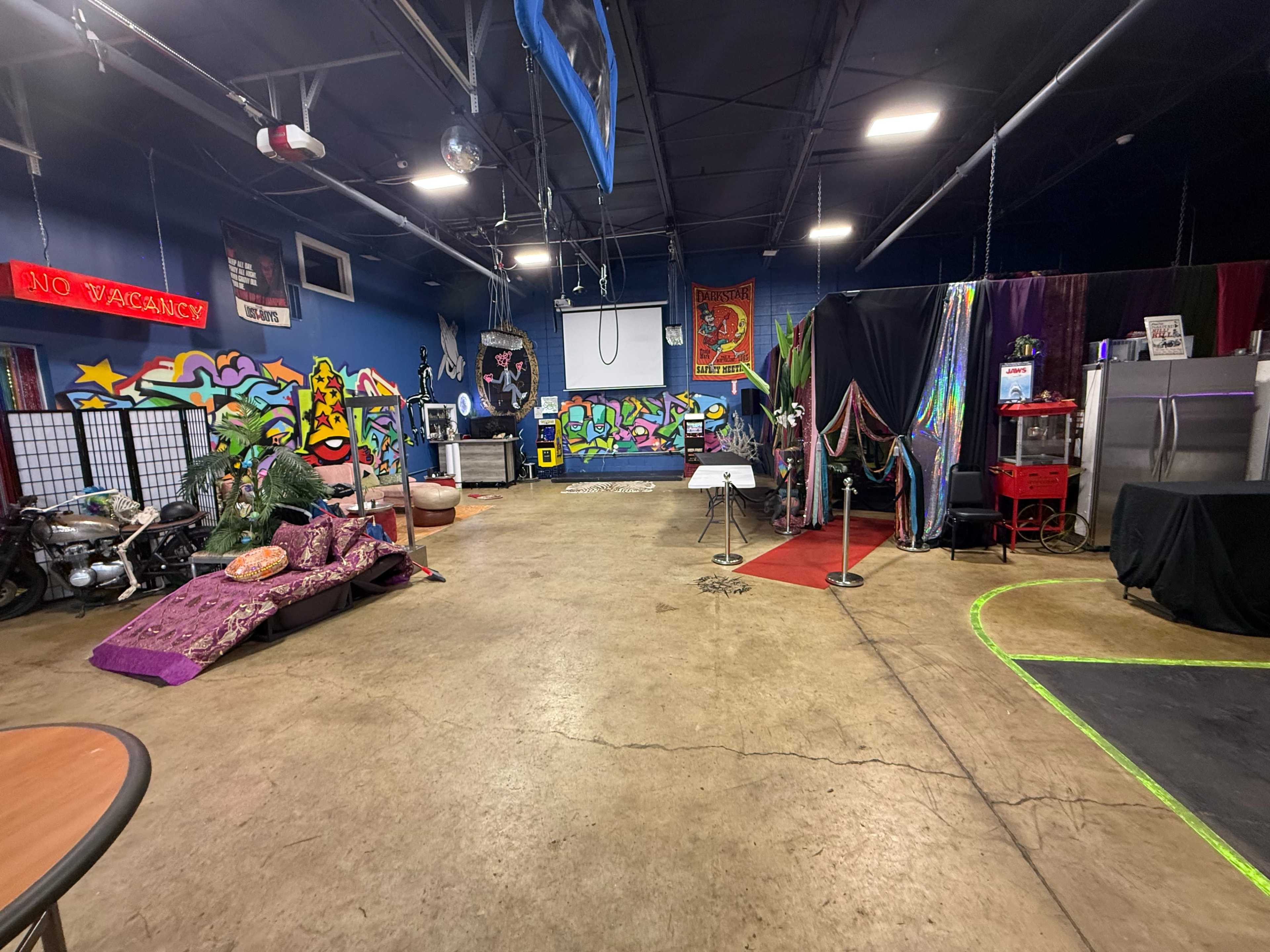 The image shows an indoor space featuring colorful graffiti on the walls, various decorations, and different areas designated for activities, including a red carpet section and a bar.