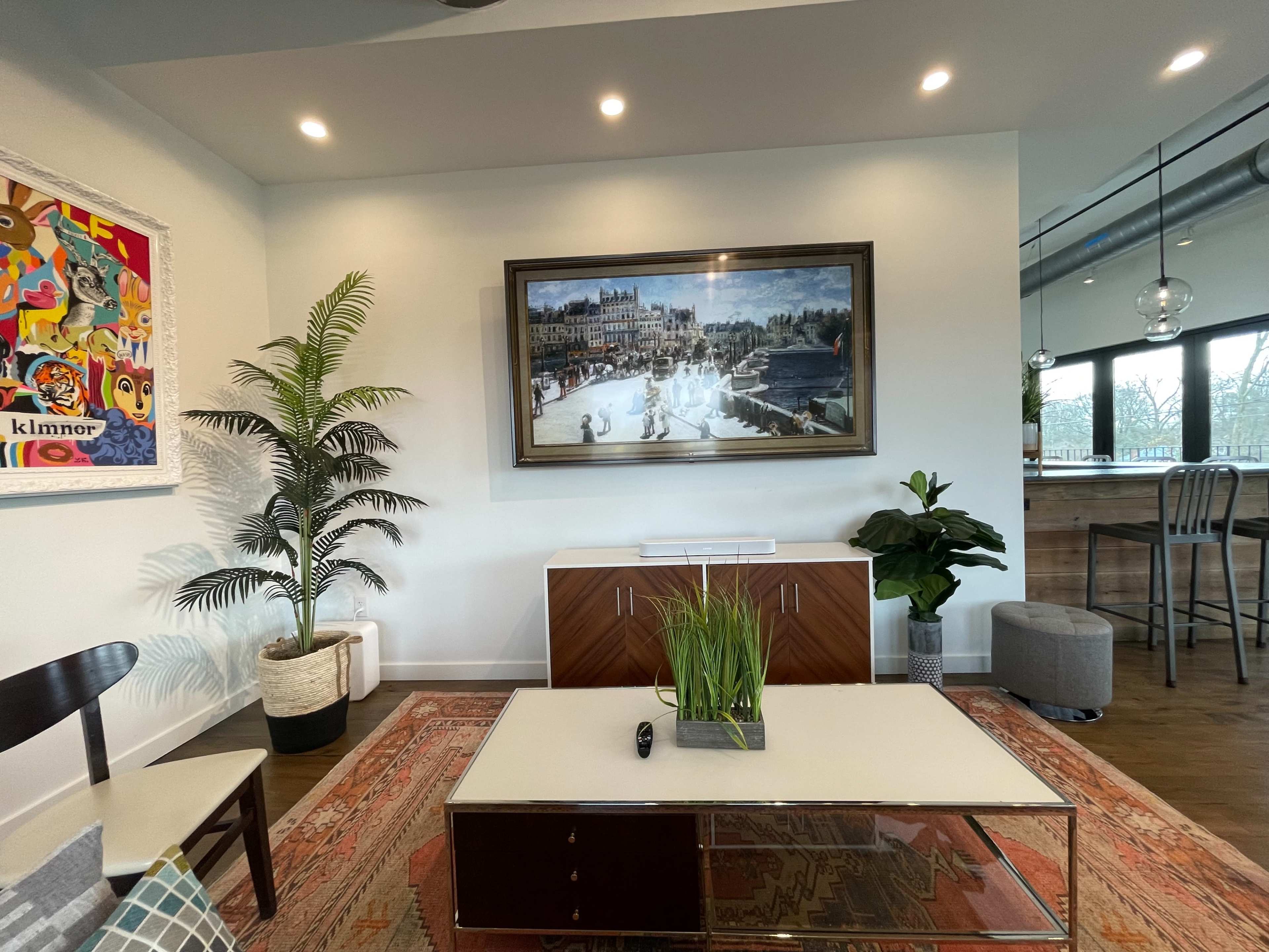 A modern living area with a large framed painting above a wooden cabinet, a potted plant, and a coffee table with a remote control, all under soft lighting.