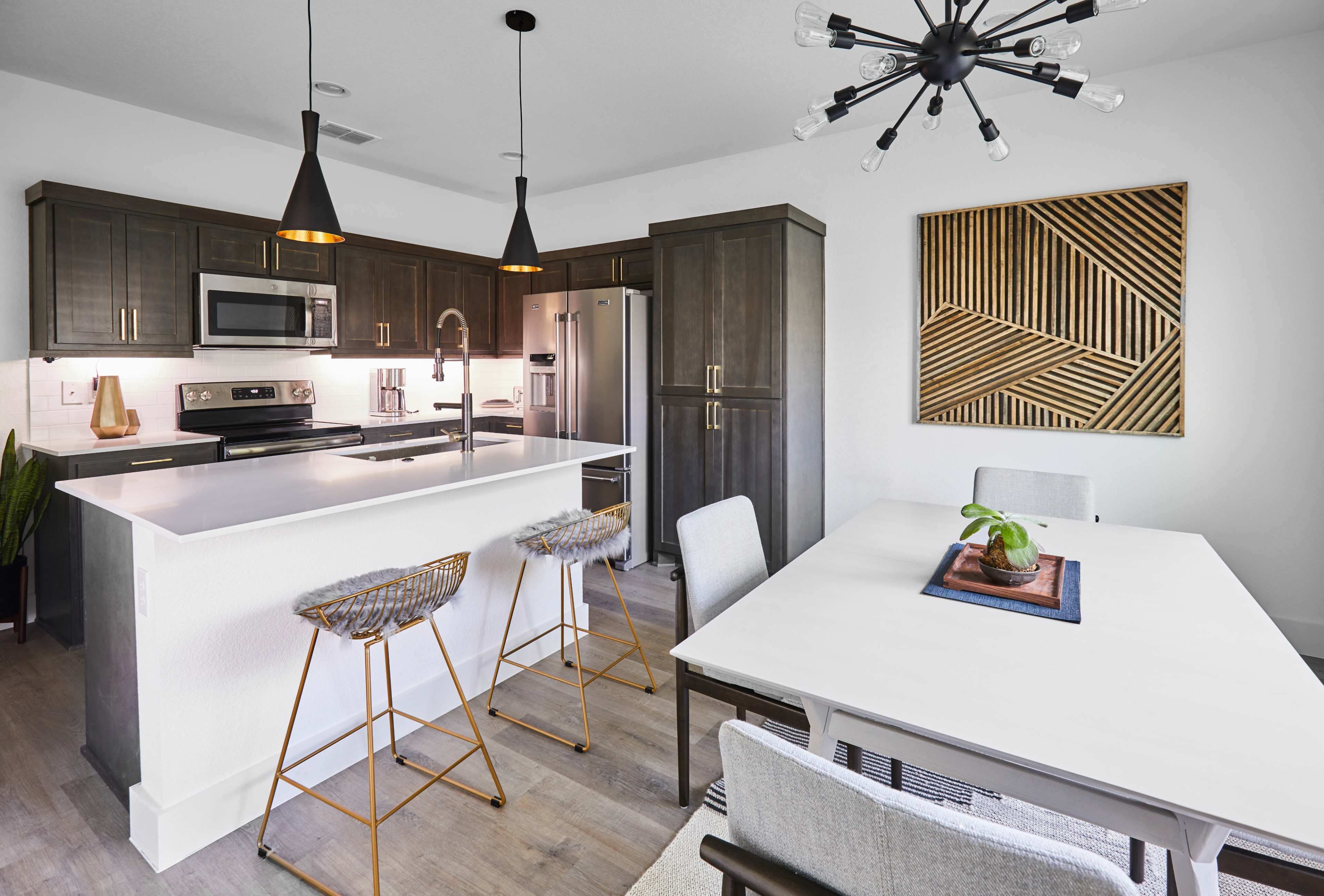 The kitchen features dark cabinetry, a white island, modern appliances, pendant lighting, and a dining area with a rectangular table and woven chairs.