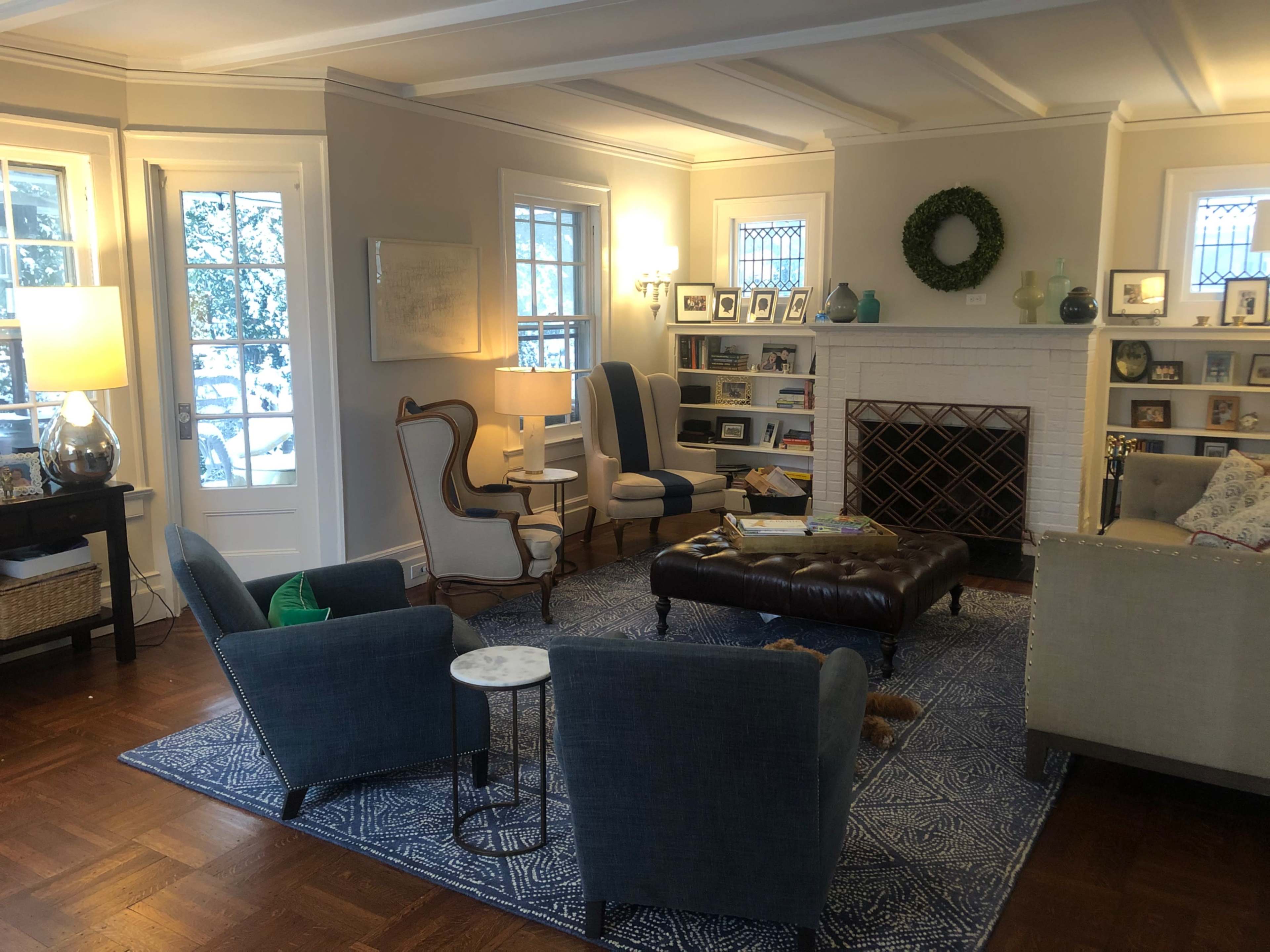 The image shows a cozy living room with a large area rug, a coffee table in the center, and various seating arrangements around a fireplace.