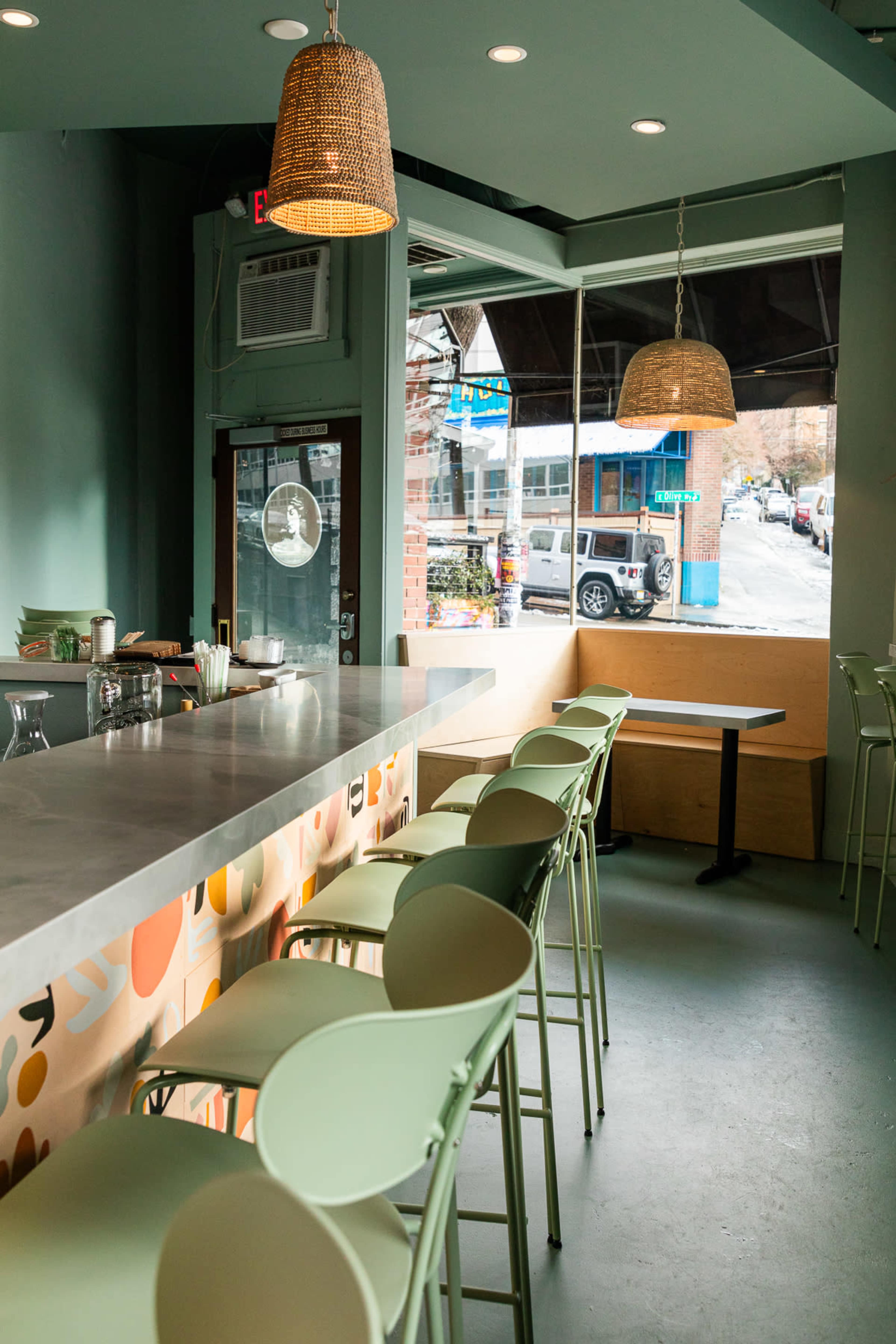 The image shows a brightly colored café interior with a clear bar area featuring light green stools and hanging wicker light fixtures.