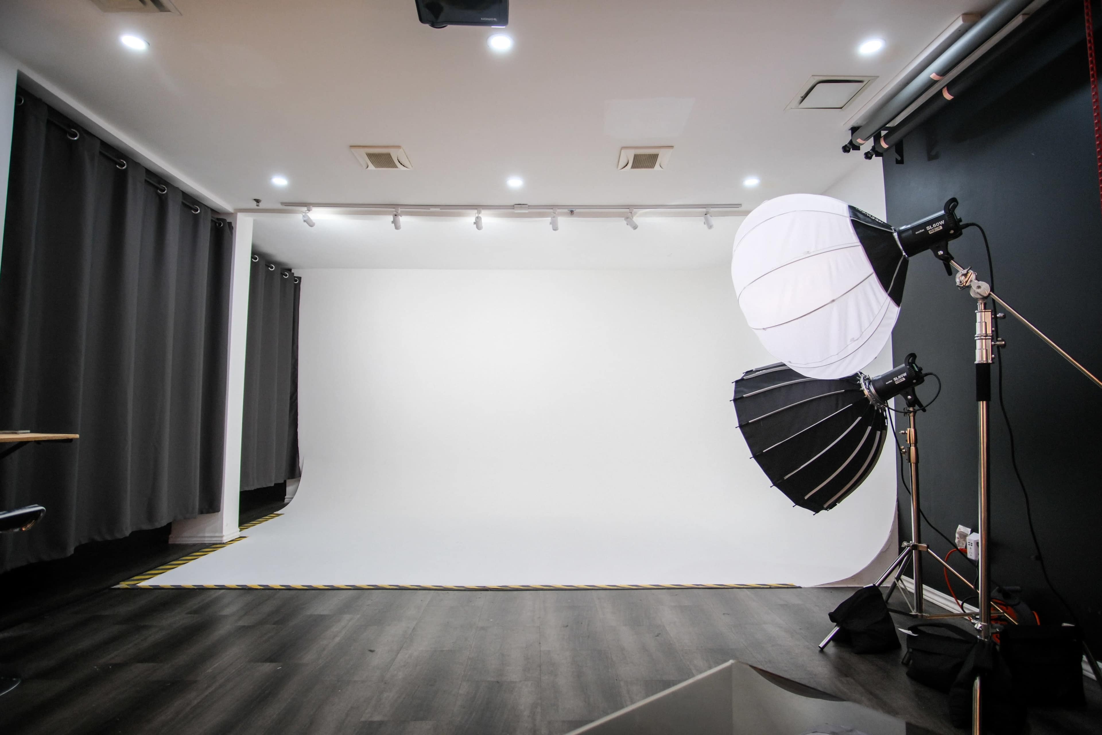 A photography studio with a white backdrop, lighting equipment, and dark curtains.