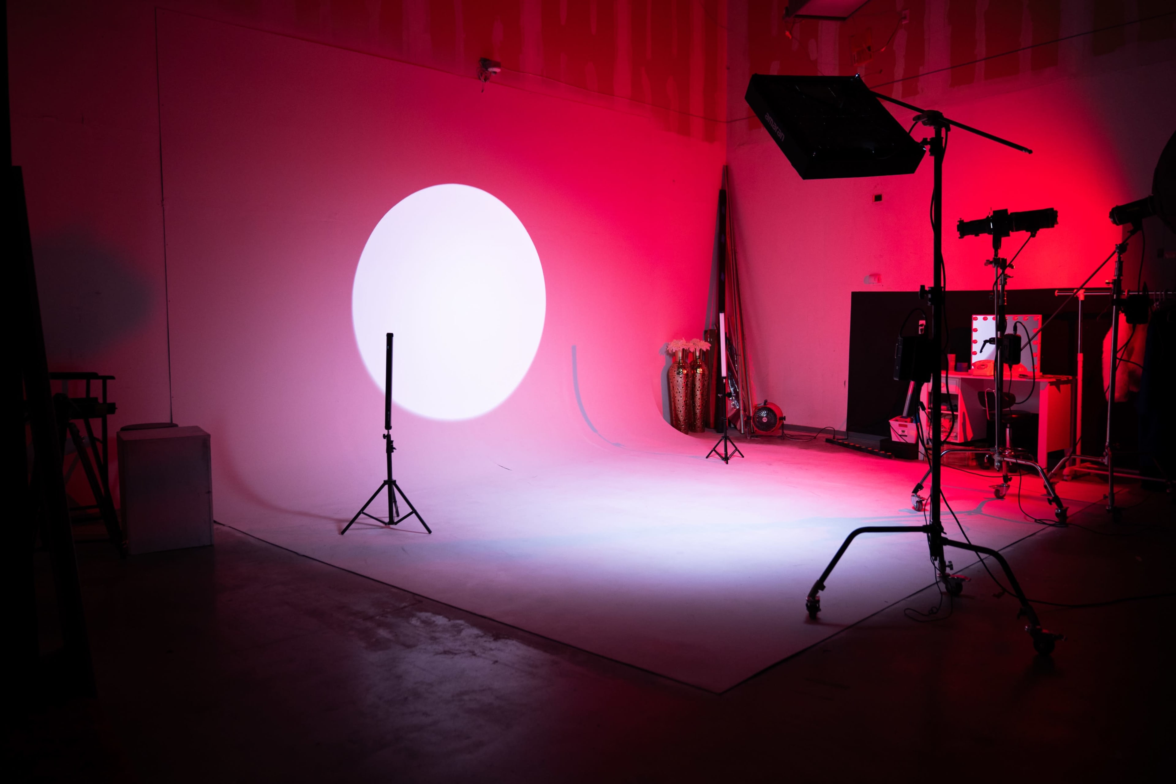 The image shows a photography studio with a large circular light projection on the wall, surrounded by various lighting equipment and a backdrop.