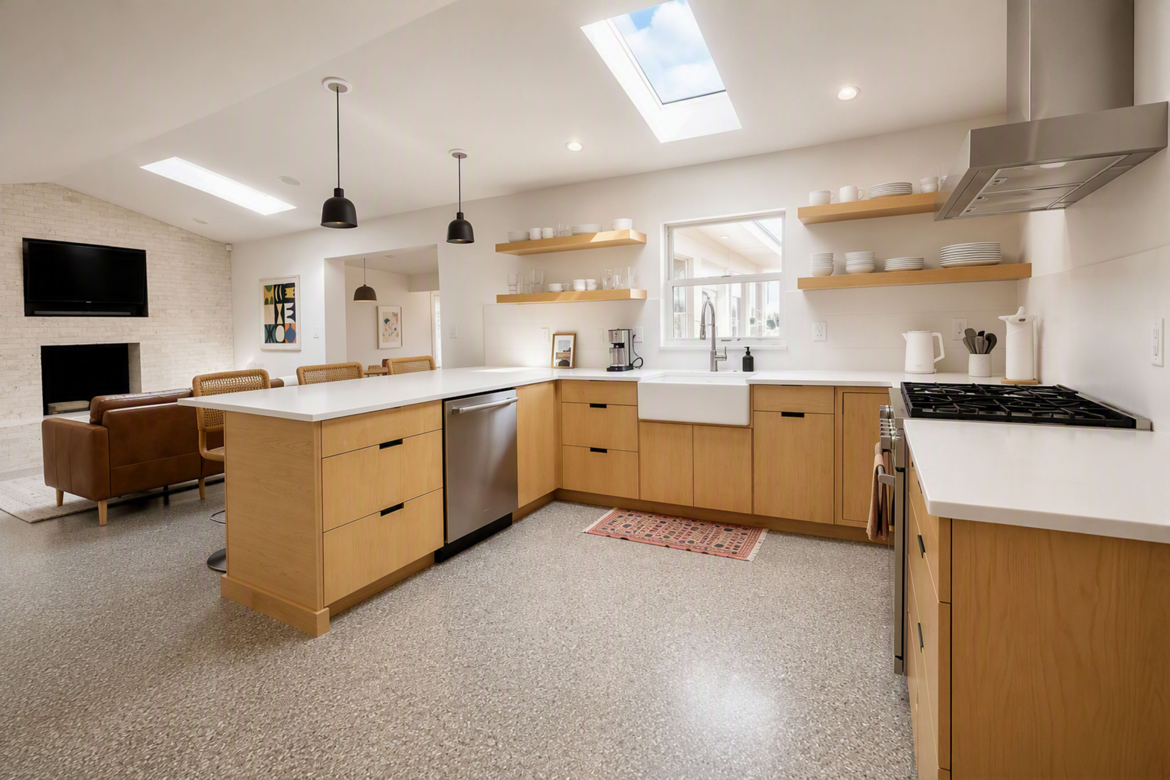 A modern kitchen features light wood cabinetry, a farmhouse sink, and stainless steel appliances, with an open layout leading into a living area.