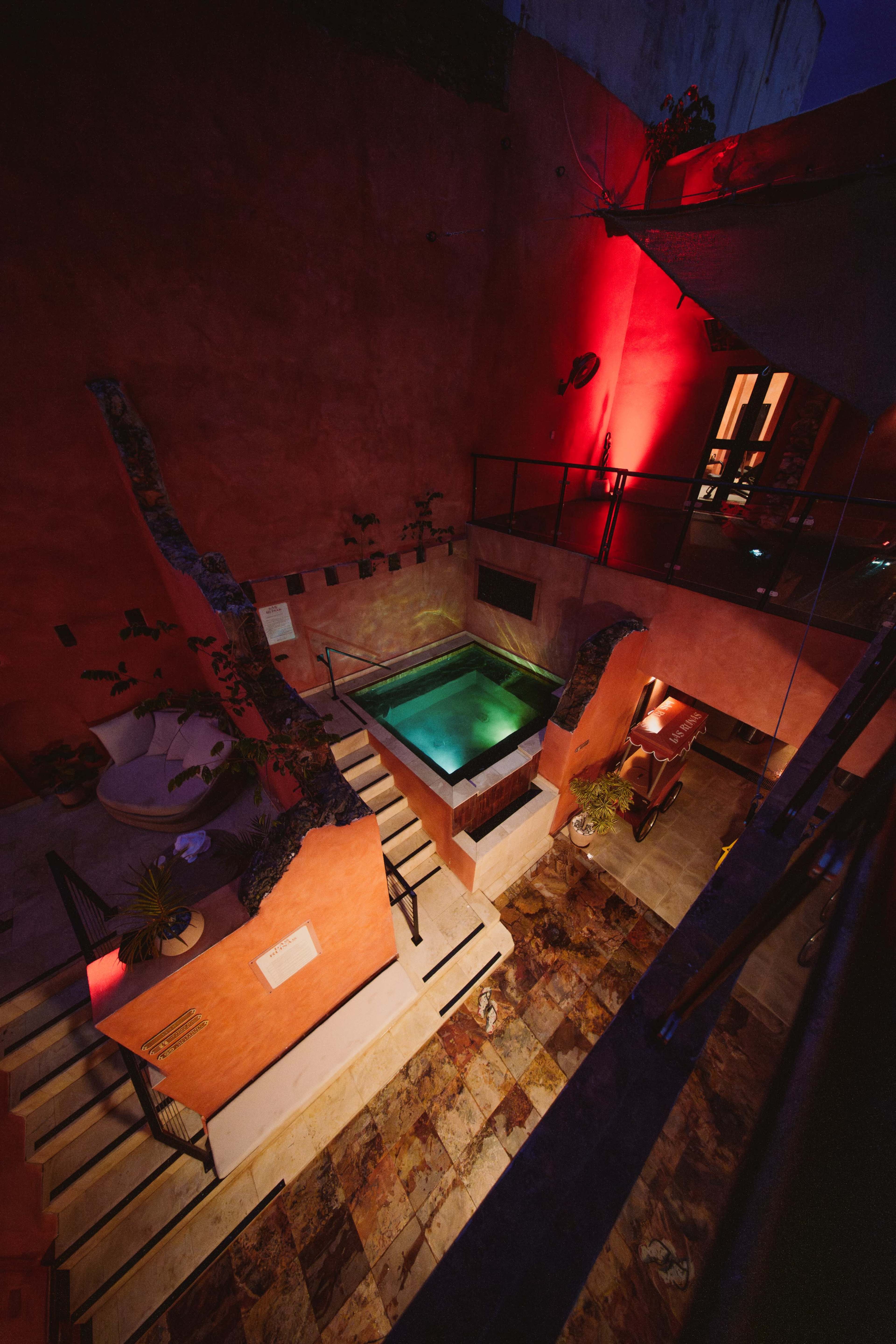 The image shows a modern indoor space featuring a small swimming pool surrounded by stairs and illuminated with red lighting.