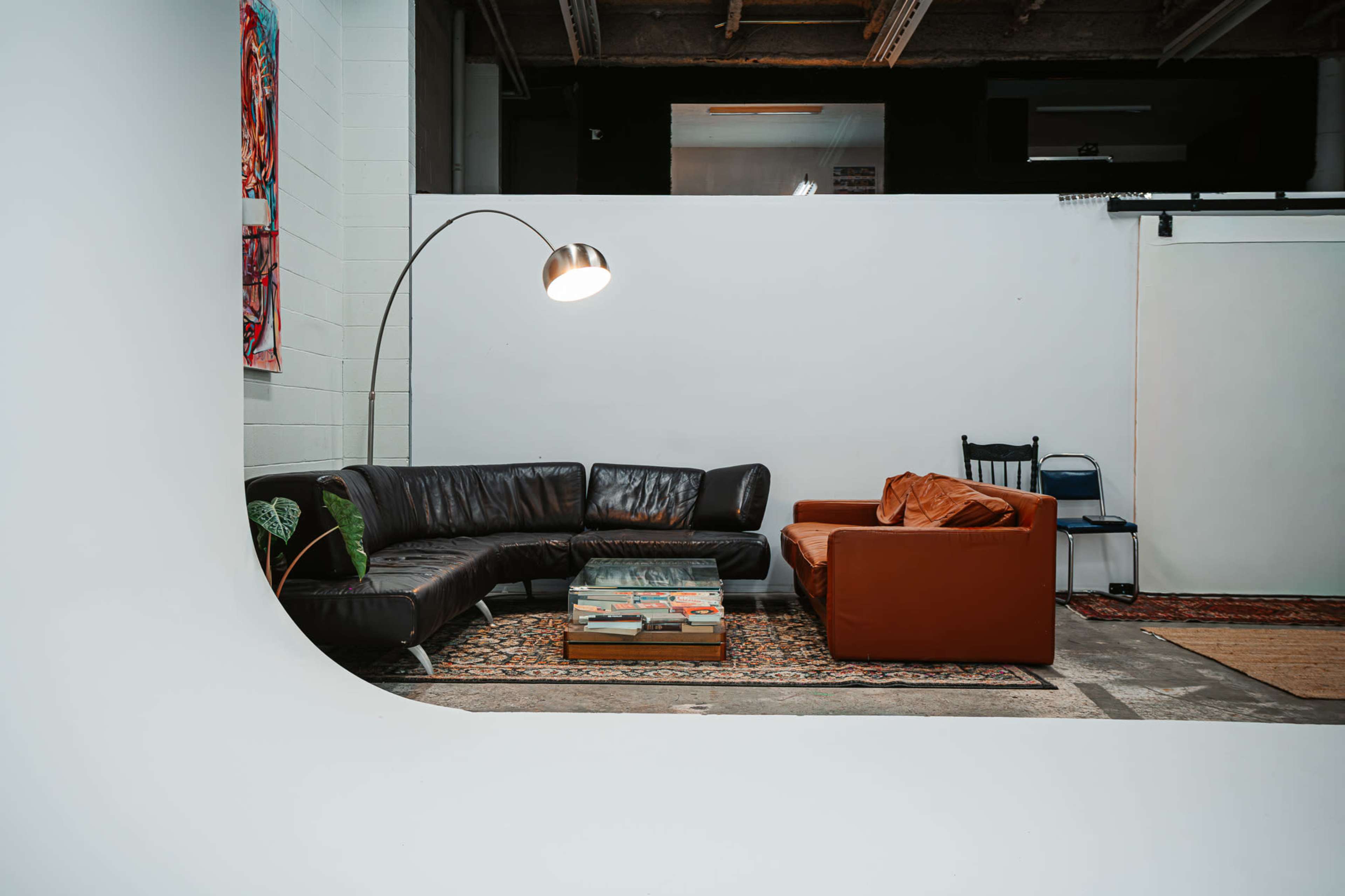 The image shows a modern interior space featuring a leather sectional sofa and a brown armchair arranged around a coffee table, with a floor lamp illuminating the area.