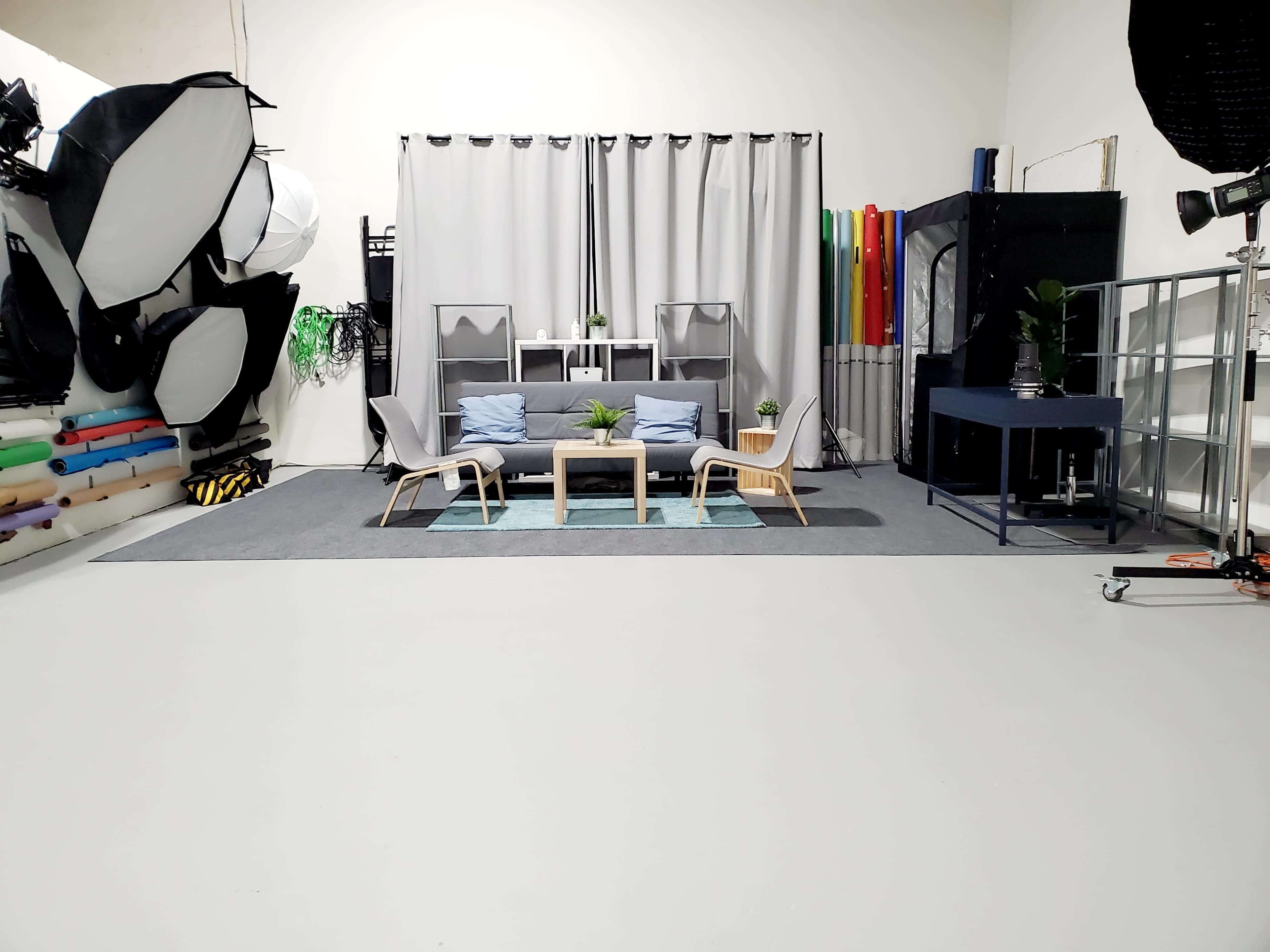 A photography studio with a set featuring a couch and chairs, surrounded by various backdrop materials and lighting equipment.