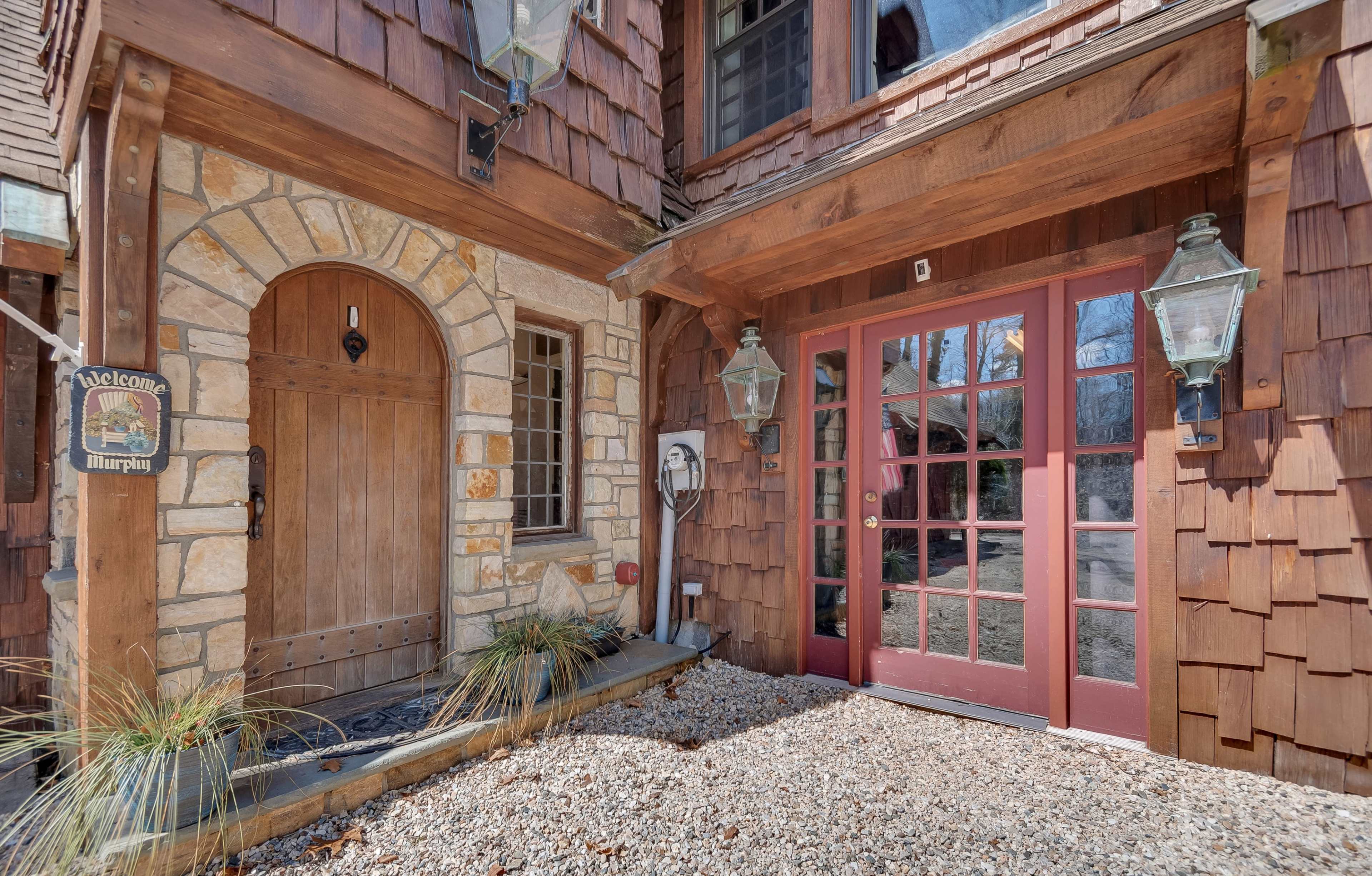 A rustic entrance featuring a wooden door with stone accents, flanked by large lanterns, leading to a house adorned with shingle siding.