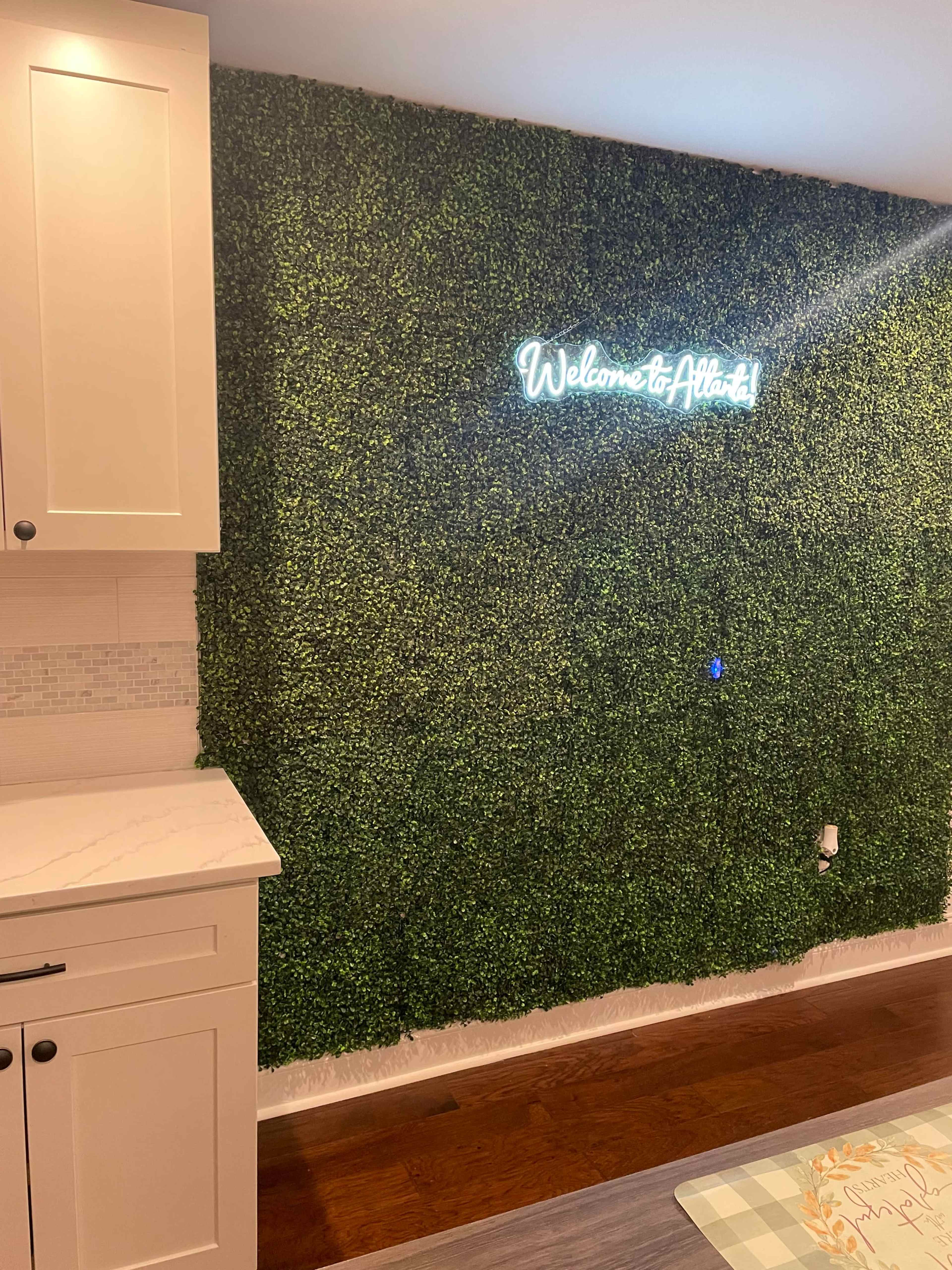 A kitchen wall covered with artificial greenery and a neon sign that reads "Welcome to Atlanta!"