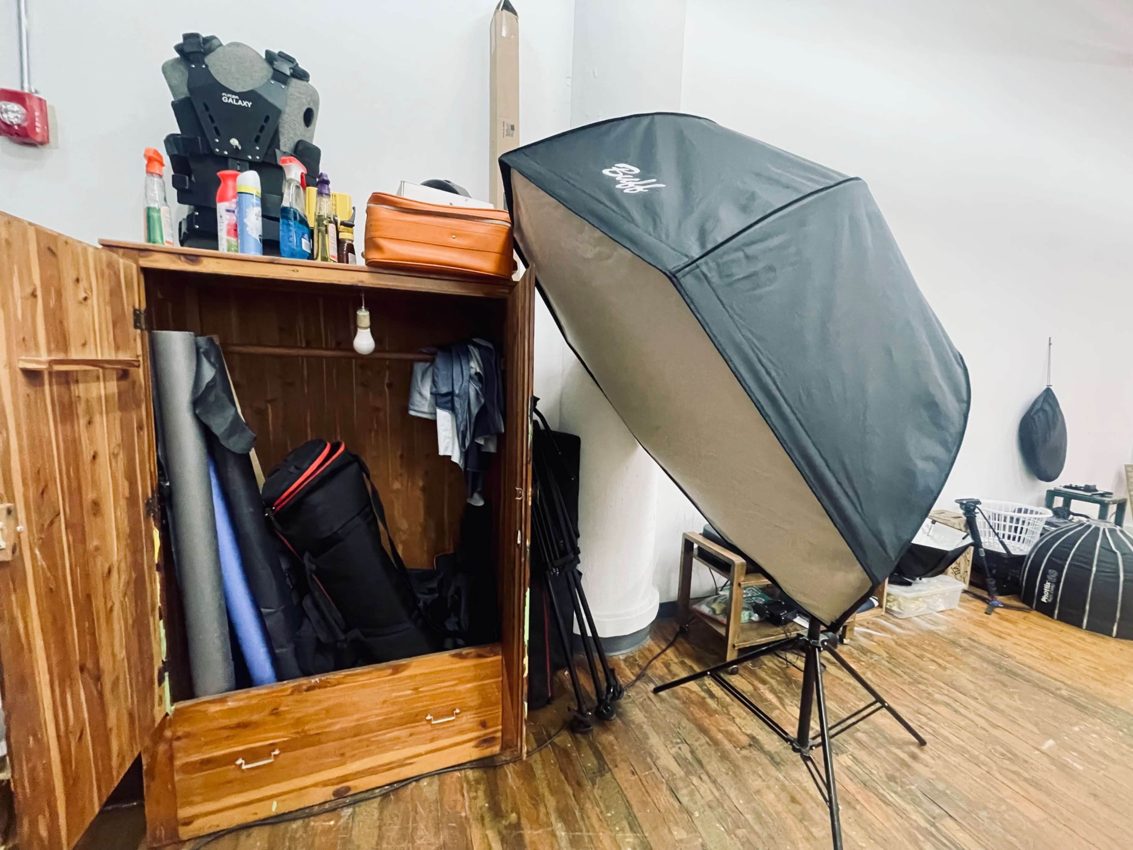 A large softbox light stands next to a wooden storage cabinet filled with photography equipment and supplies.