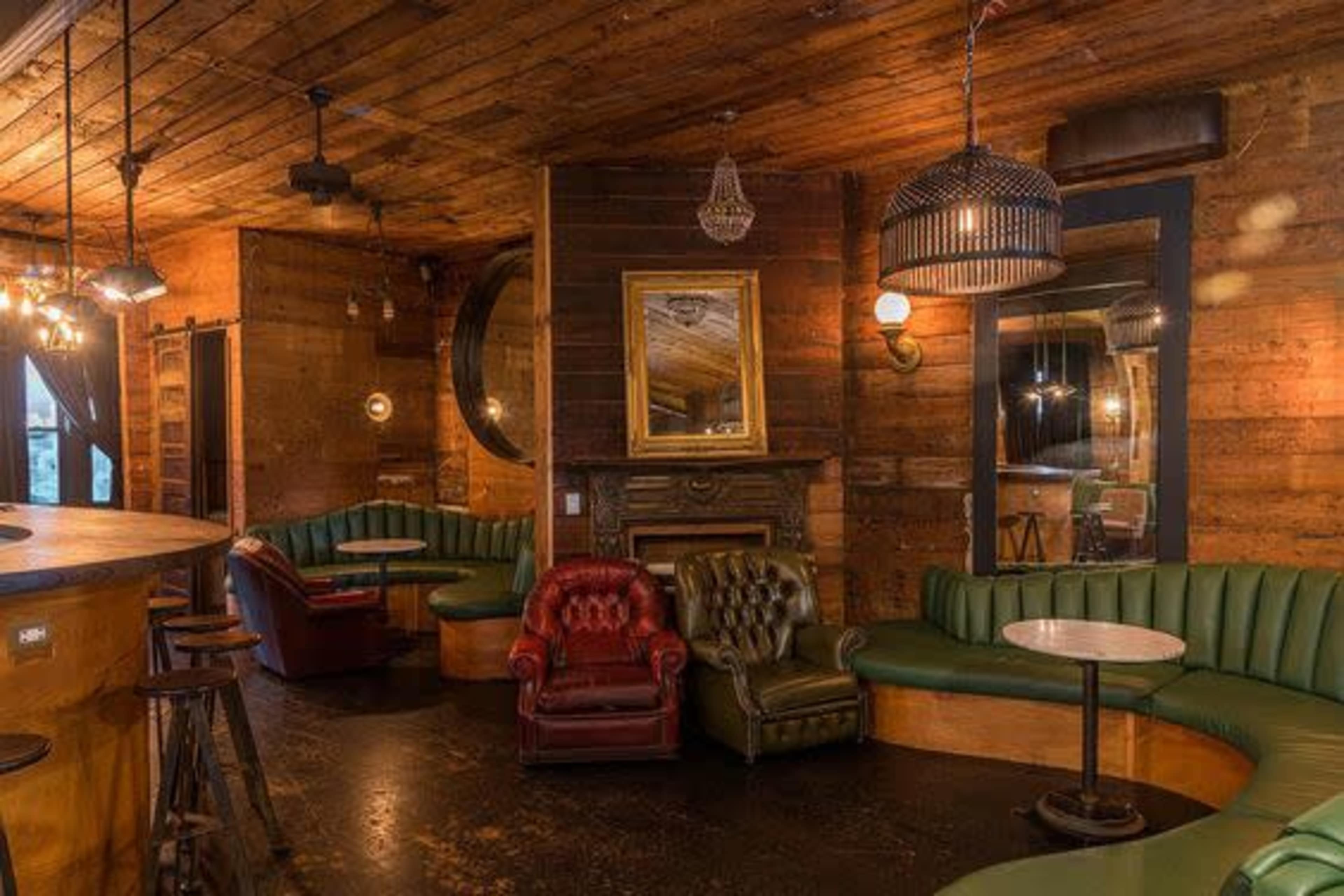 A cozy bar interior with wooden walls, plush green seating, and a mix of ambient lighting fixtures.