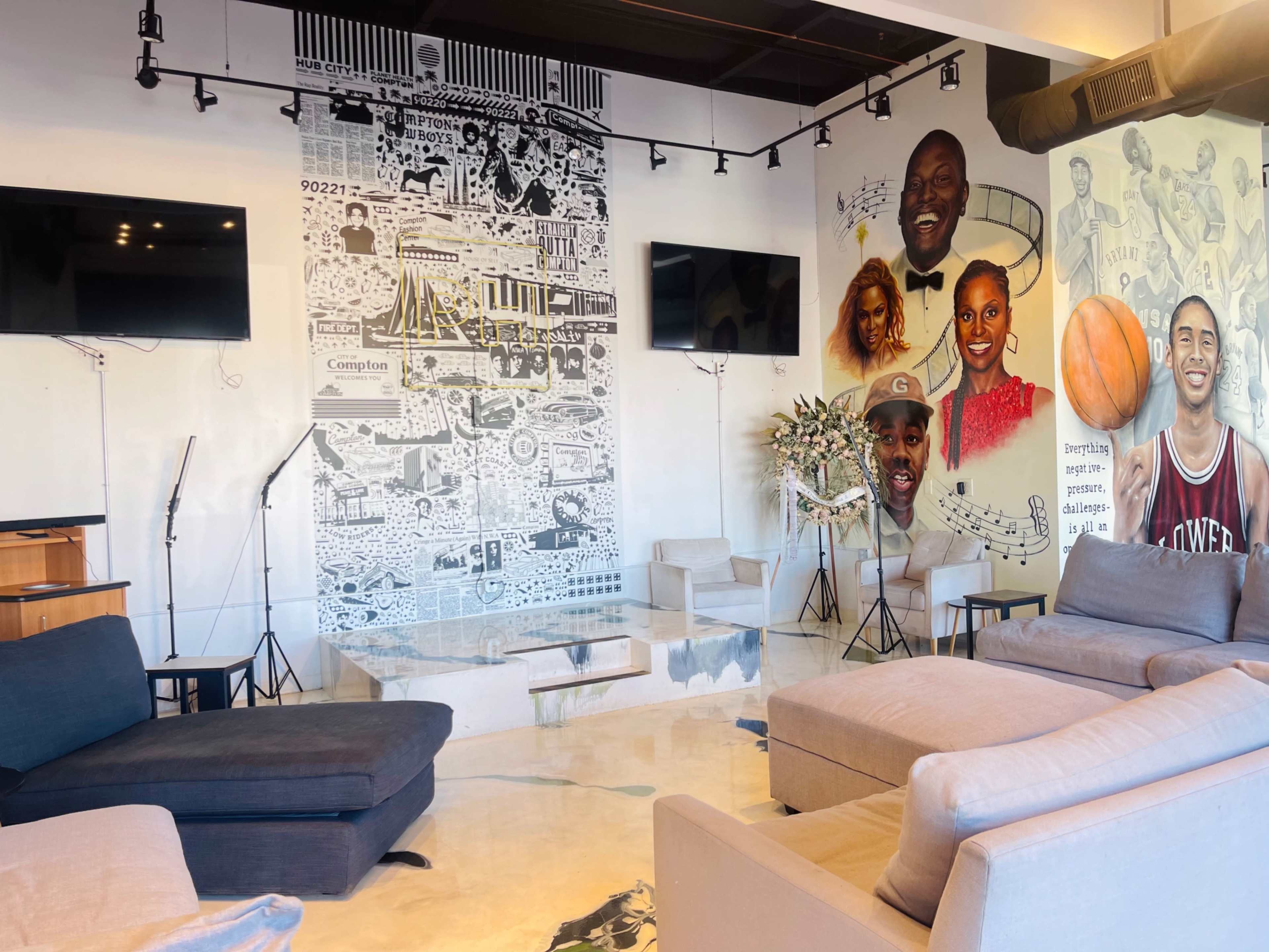 The room features a vibrant mural wall with images and text, two flat-screen TVs, and comfortable seating arrangements.