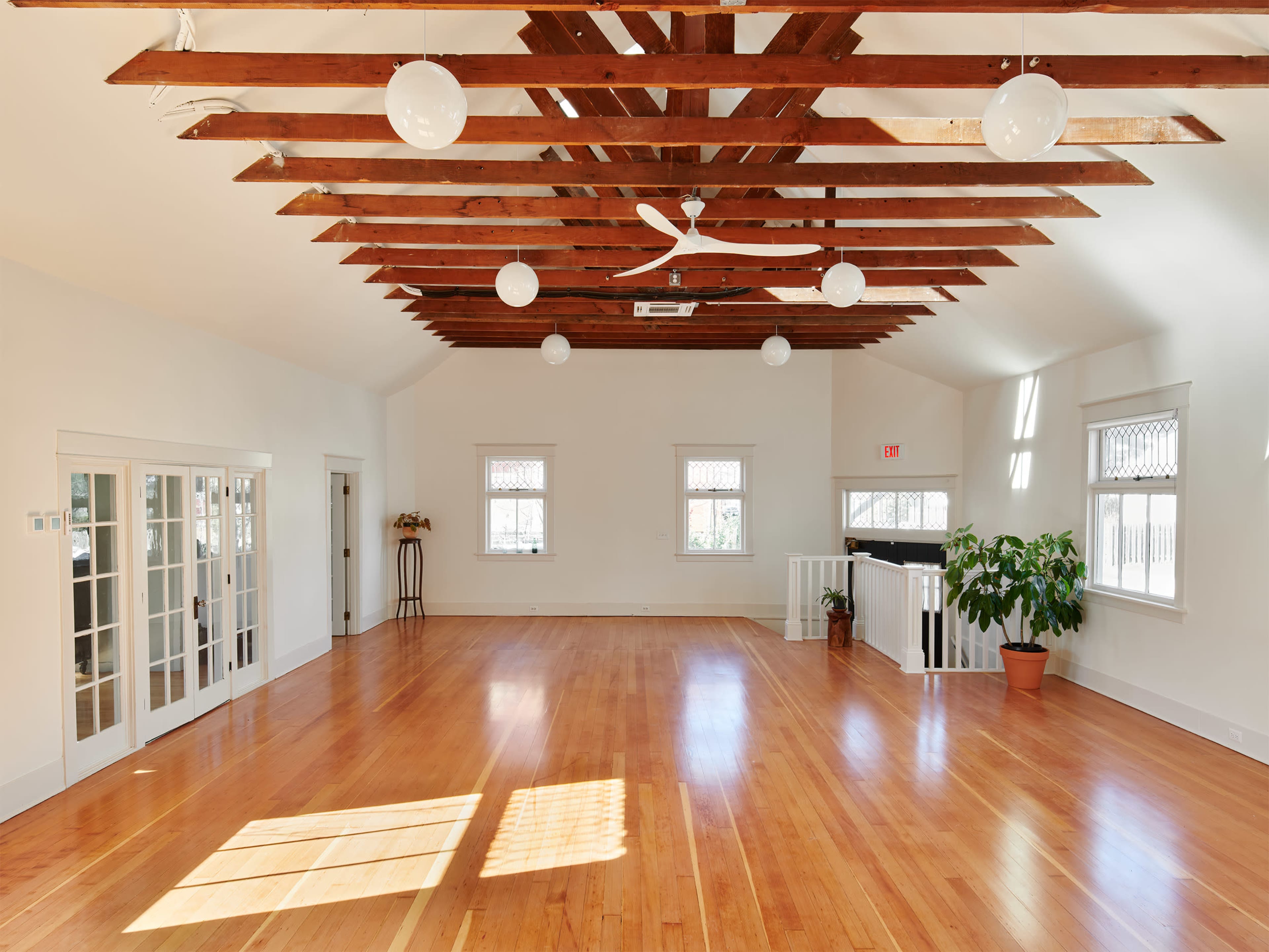 A spacious interior room with hardwood flooring, exposed wooden beams, and large windows allowing natural light.