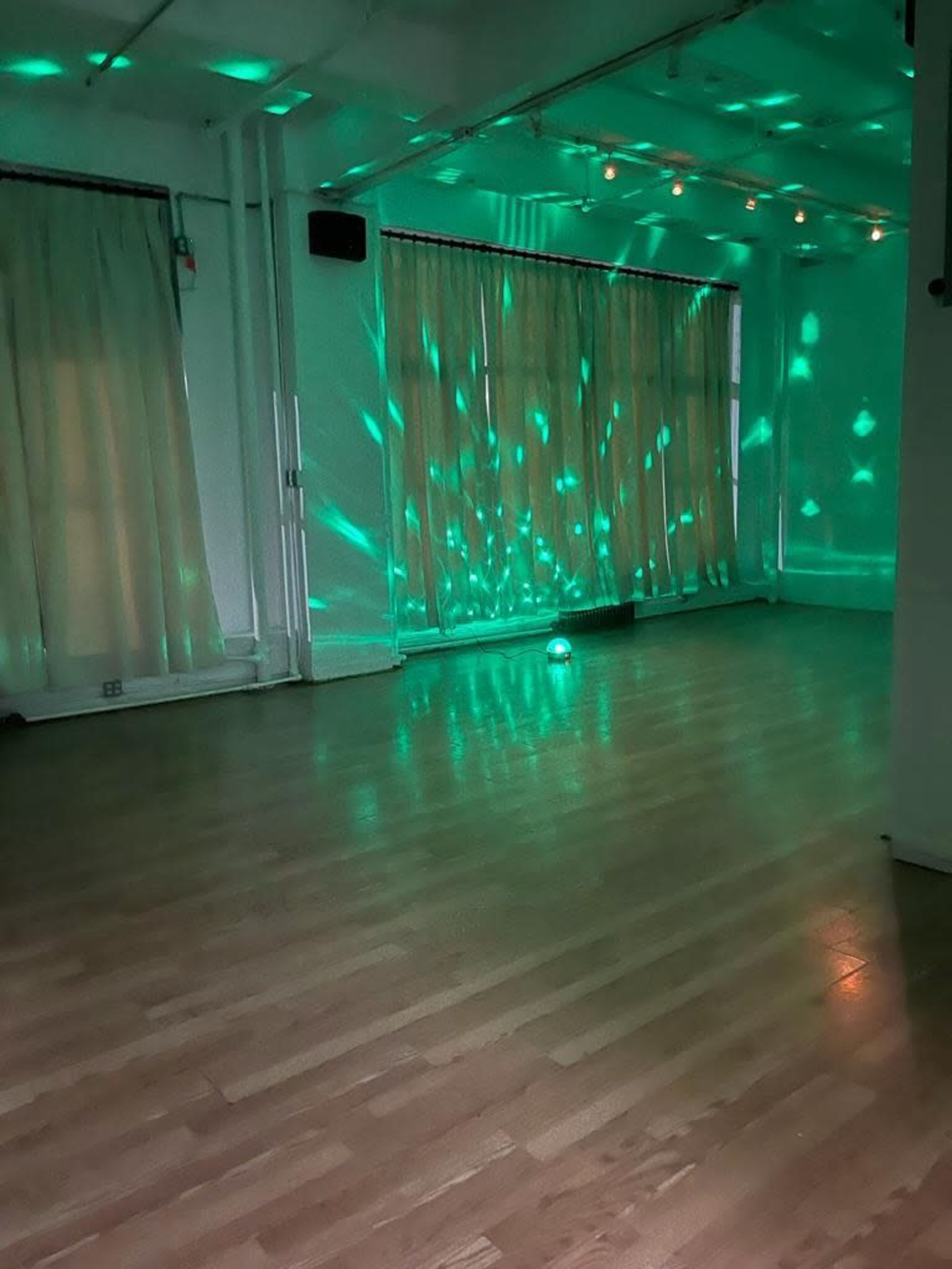 A spacious room with wooden floors, lit by green lighting patterns projected on the walls and curtains.