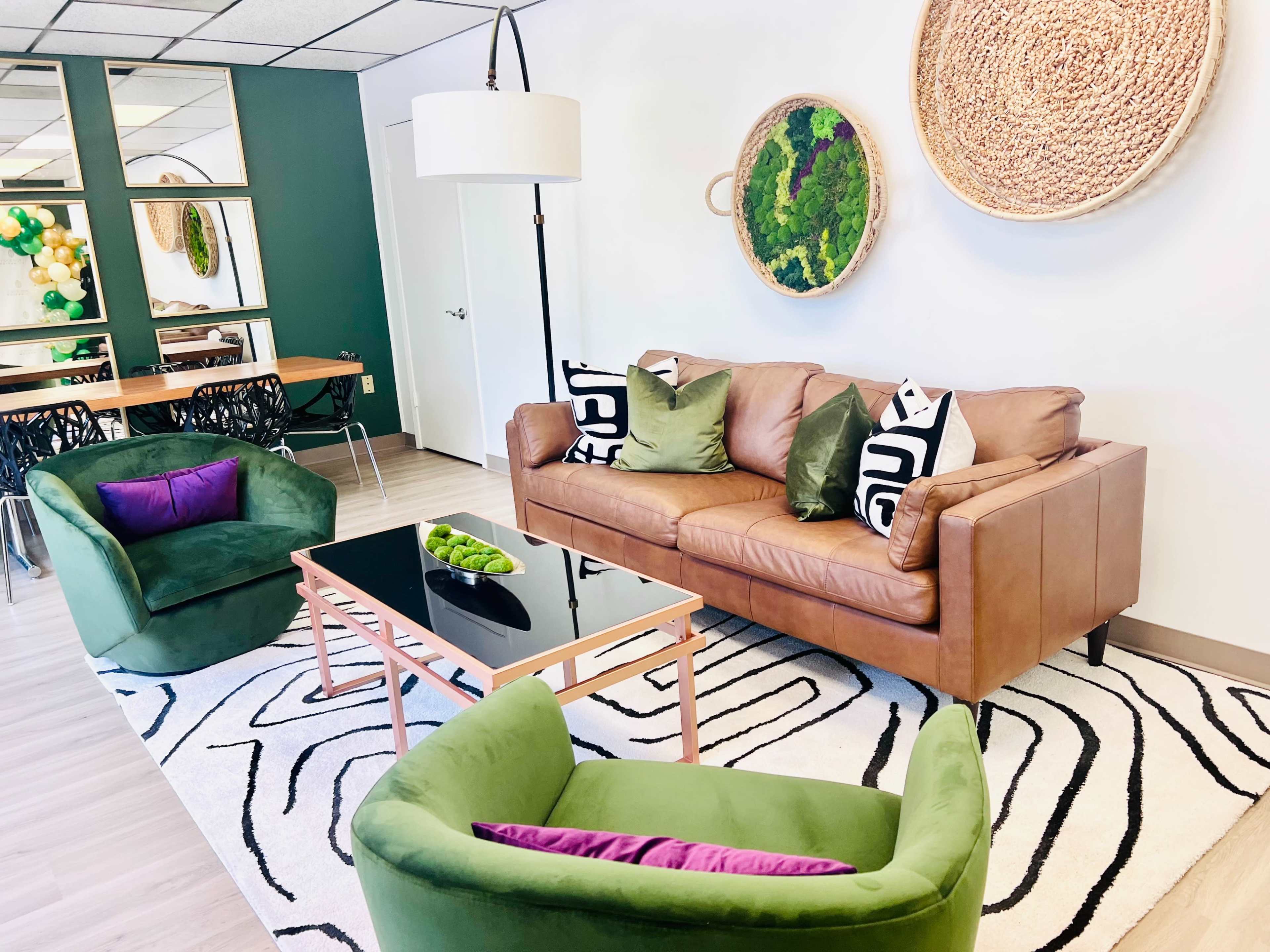 The image shows a modern living room featuring a brown leather sofa, two green armchairs, a black coffee table, and decorative wall art.