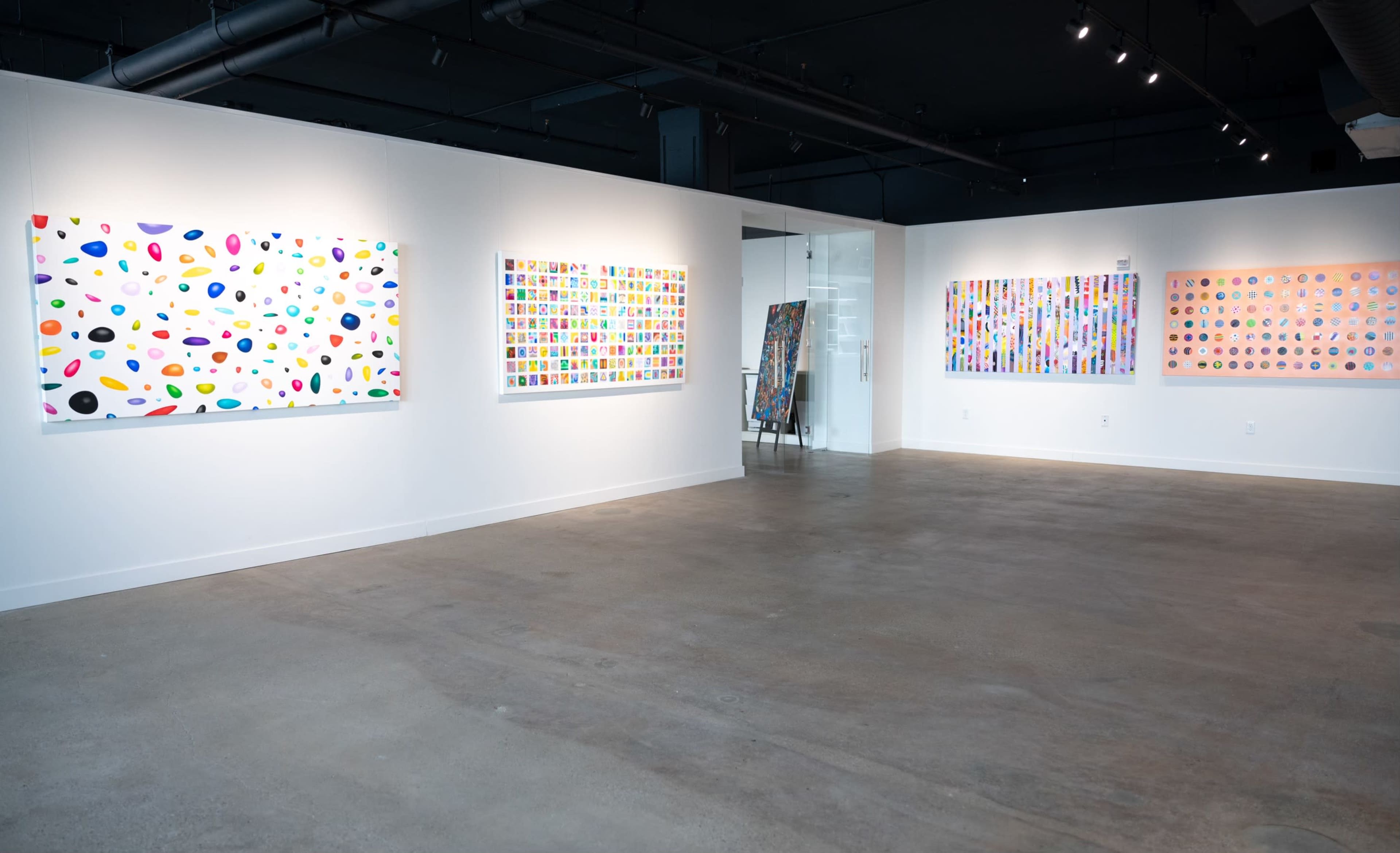 The image shows an art gallery featuring several colorful abstract paintings on the walls and a clear floor space.