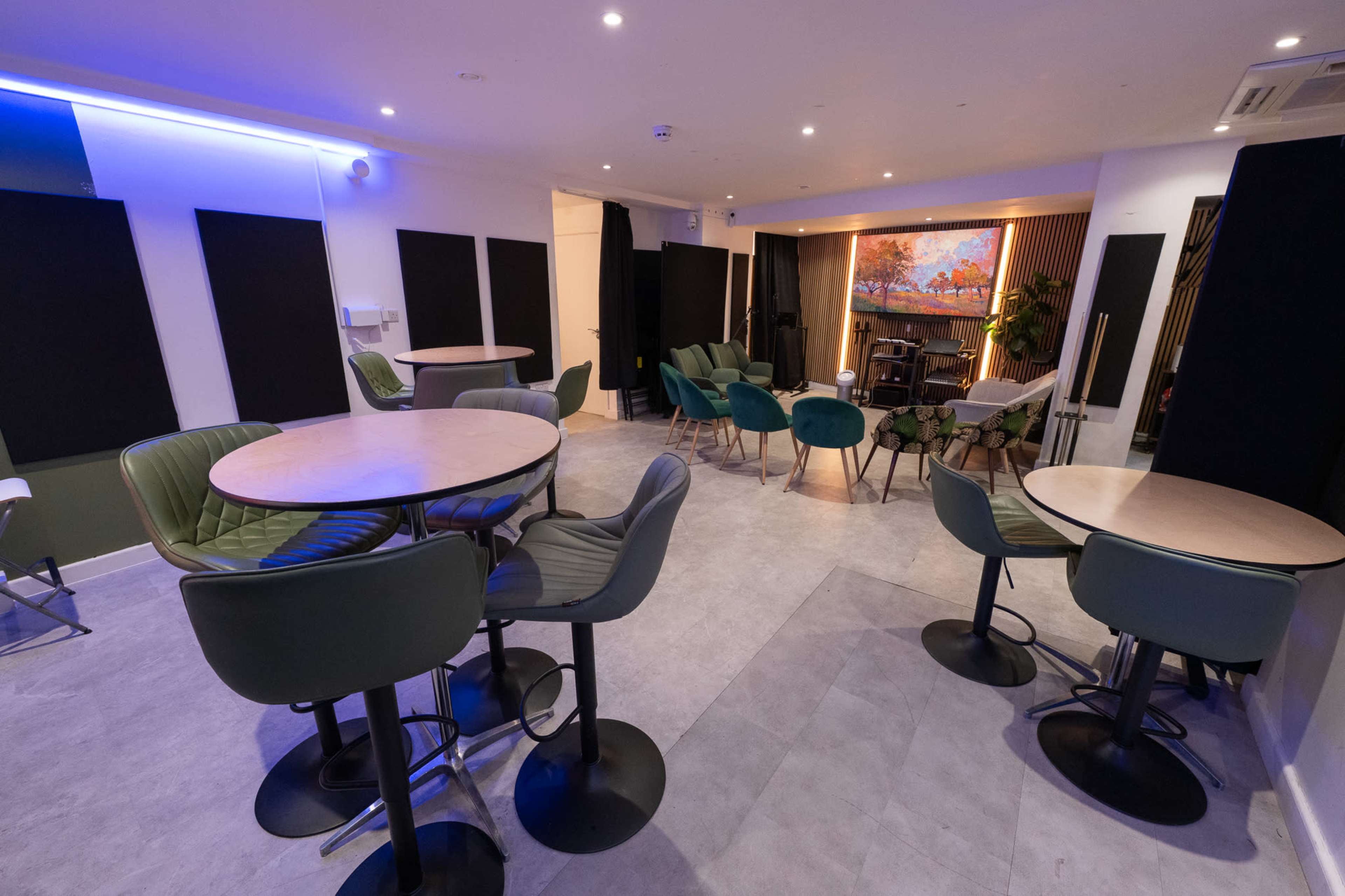 The image shows a modern interior space with several tables and chairs arranged, featuring a large screen displaying a scenic landscape and soundproofing panels on the walls.