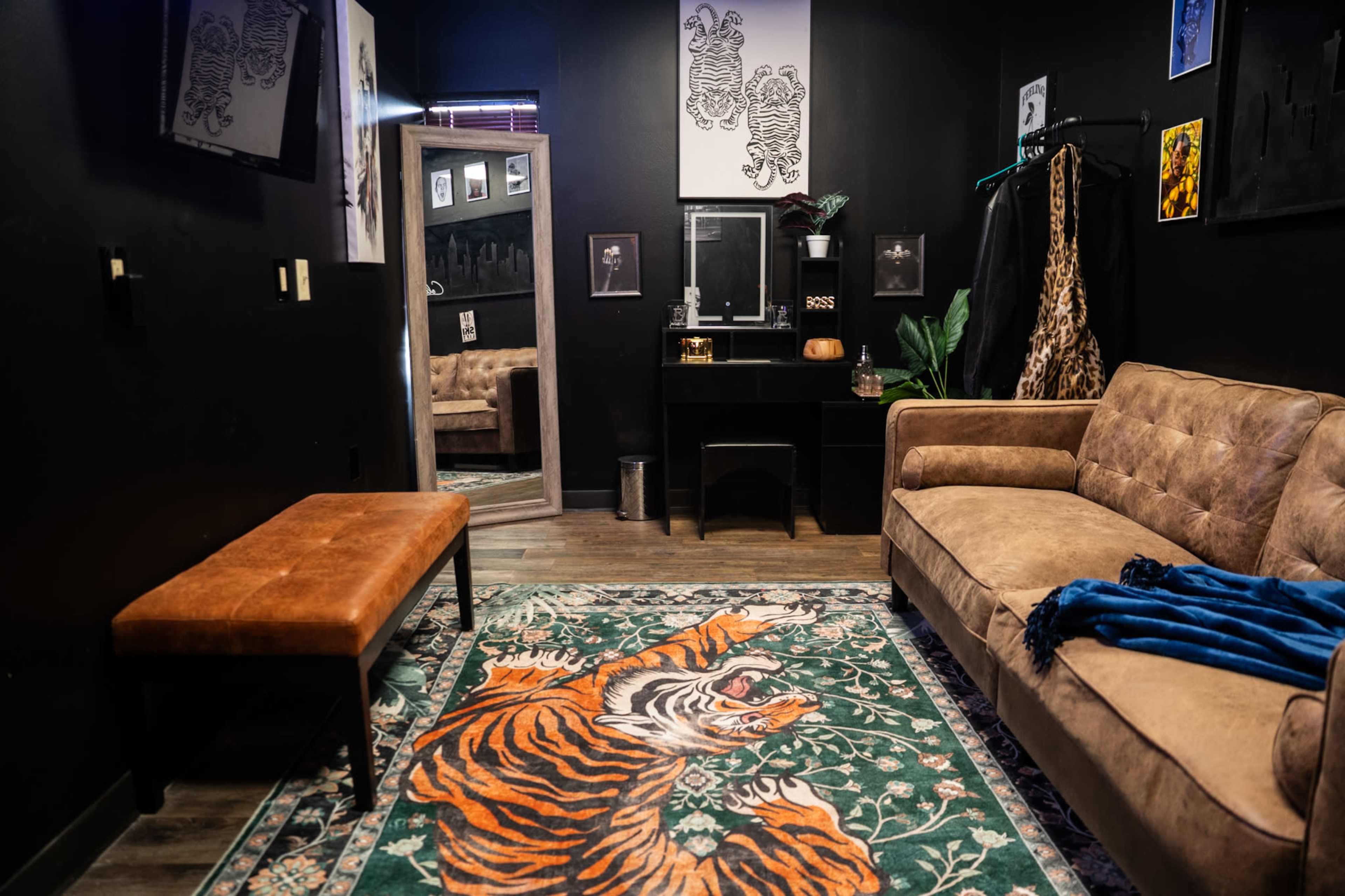 The room features a brown sofa and a wooden bench on a patterned rug with a tiger design, surrounded by dark walls and framed artwork.